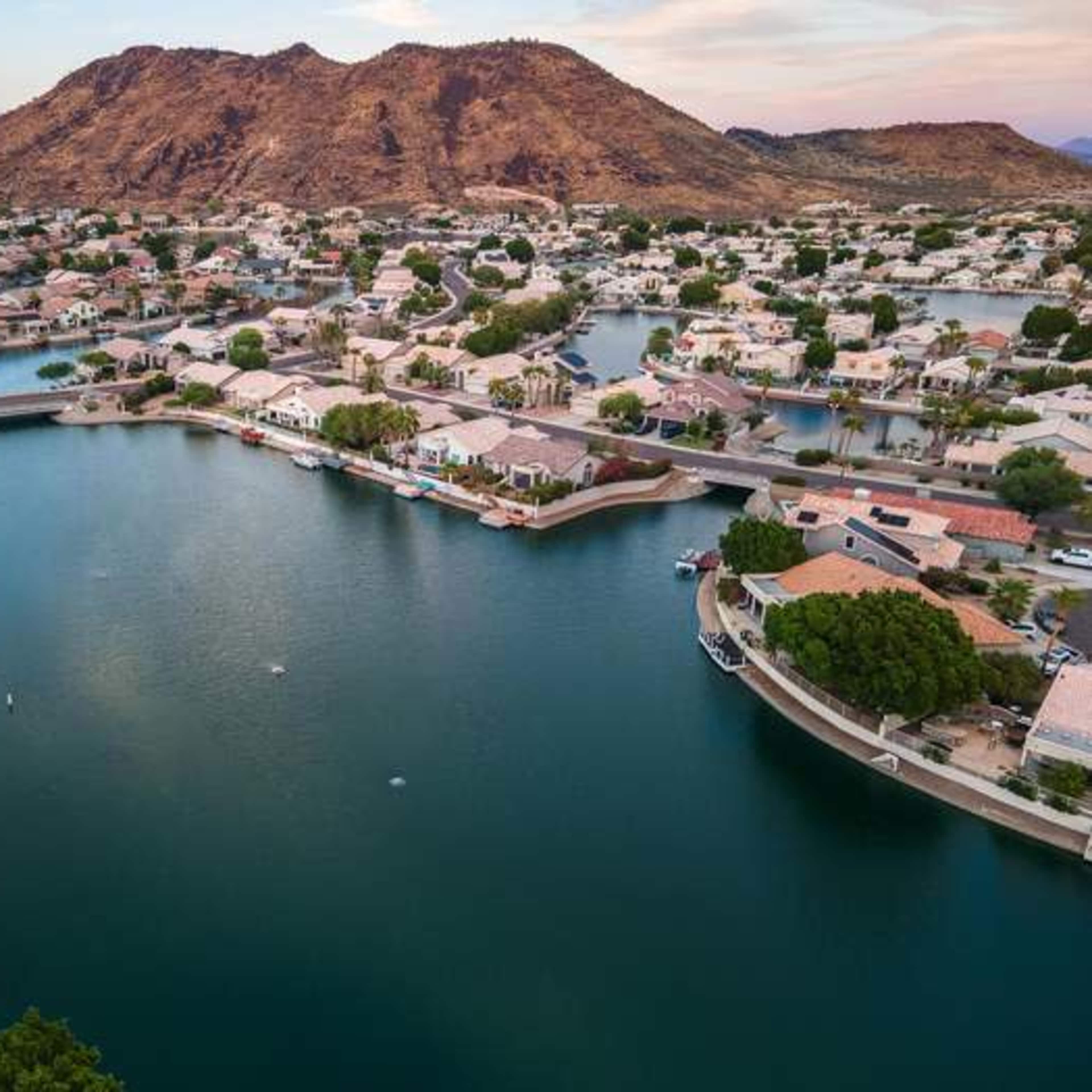 A scenic aerial view of a residential area with houses along a series of canals, set against a backdrop of a mountain.