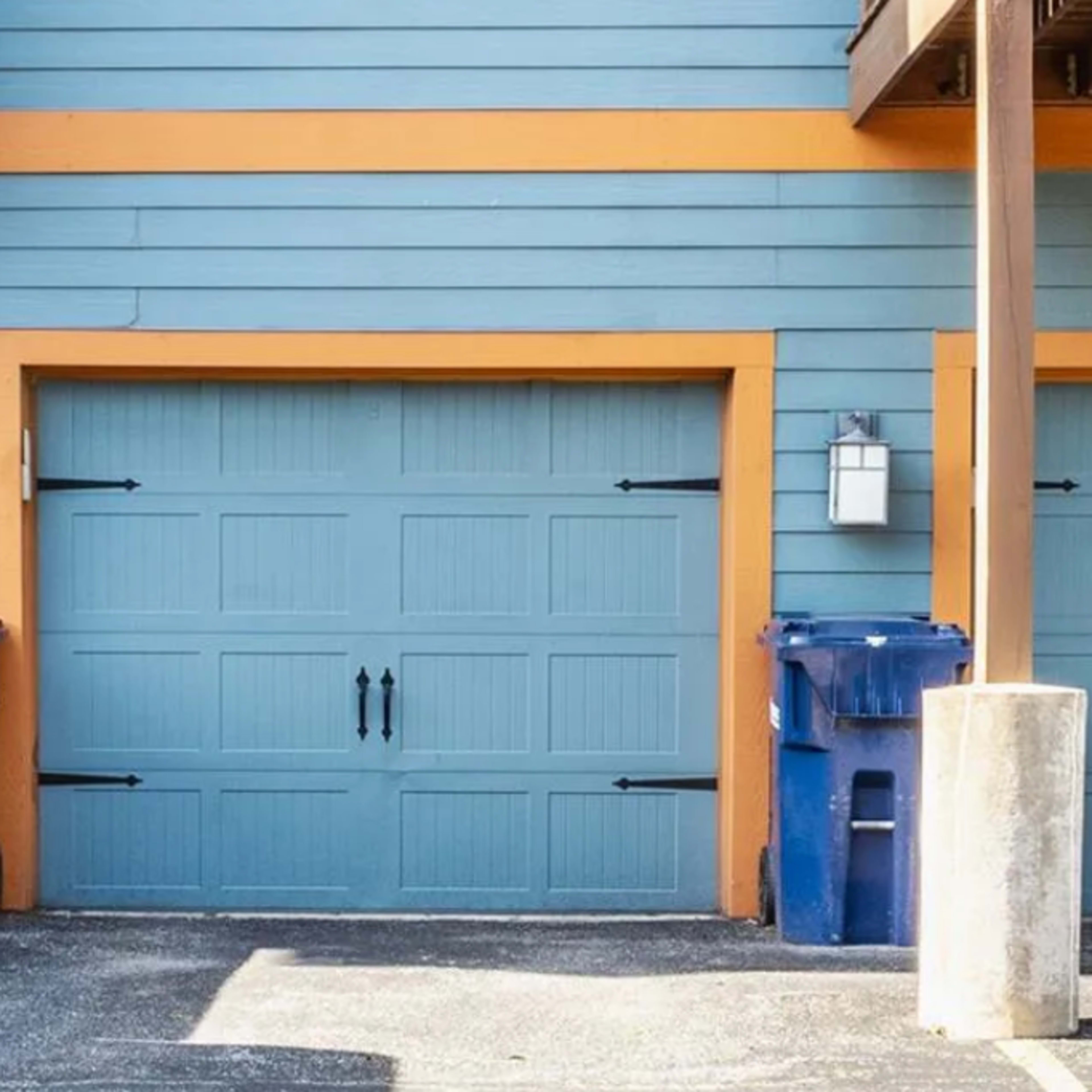 A blue garage door framed by orange trim, flanked by two blue garbage bins on either side.