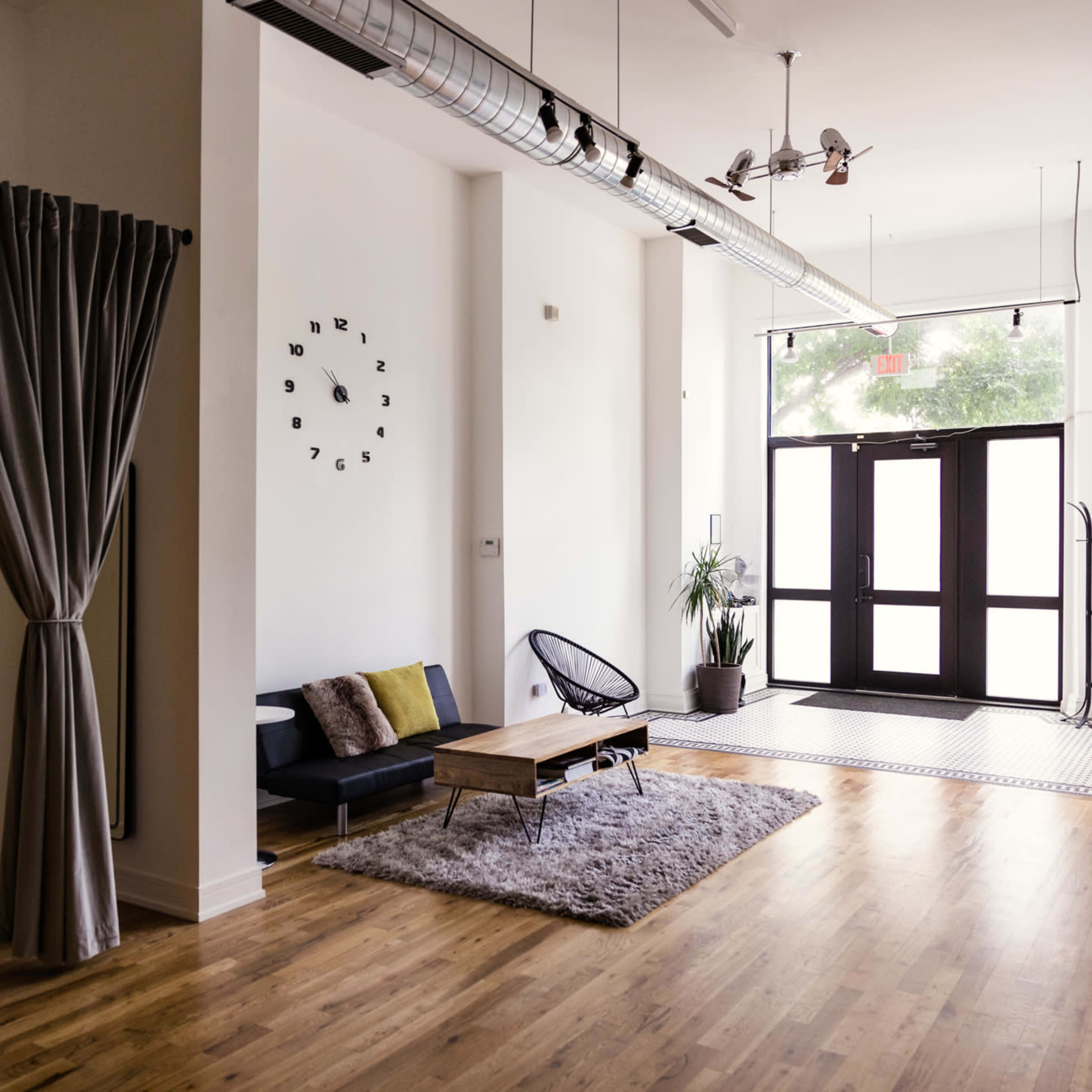 A spacious, minimalist room featuring a seating area with a sofa and coffee table, large windows, and decorative curtains.