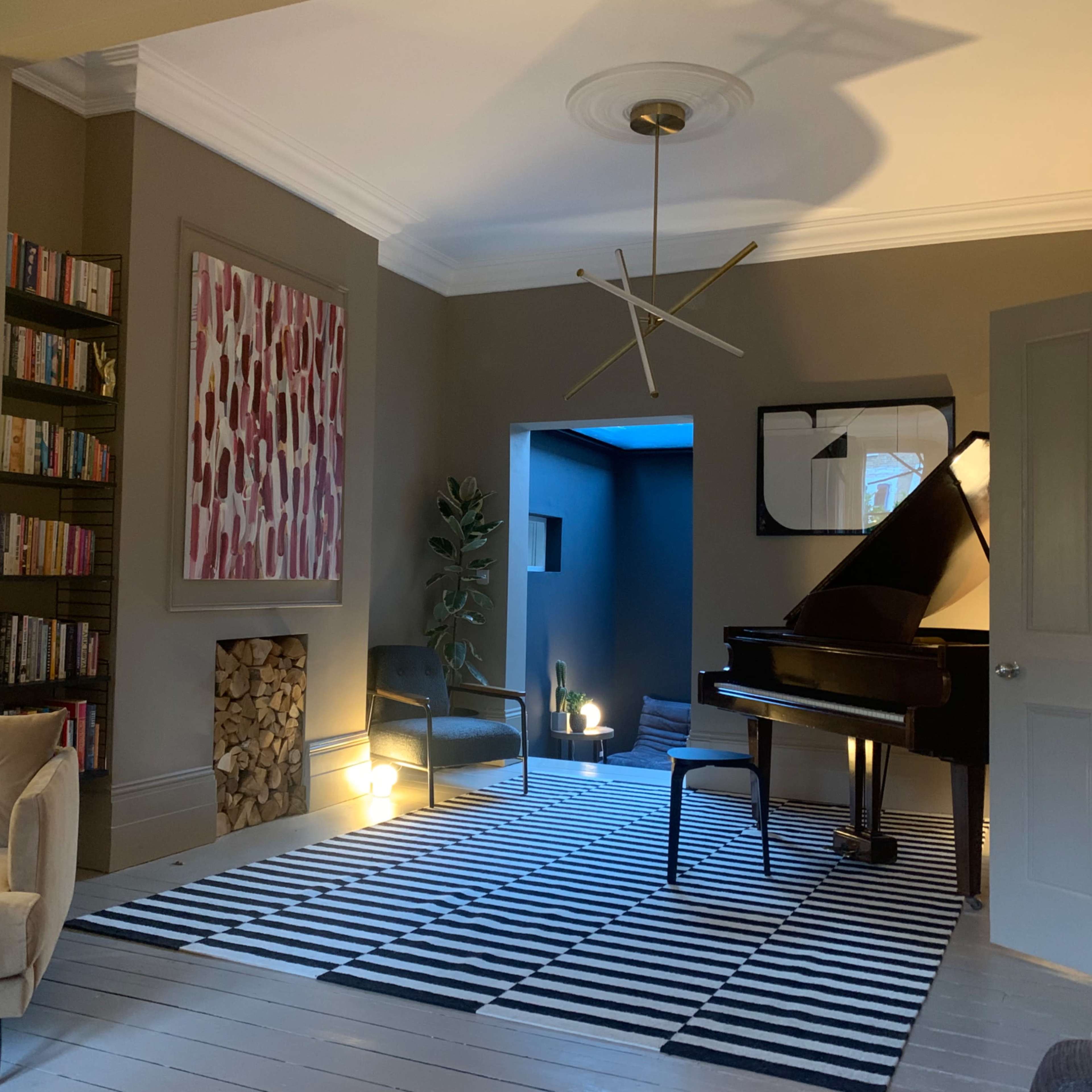 A living room featuring a grand piano, a striped rug, bookshelves, and a modern chandelier.