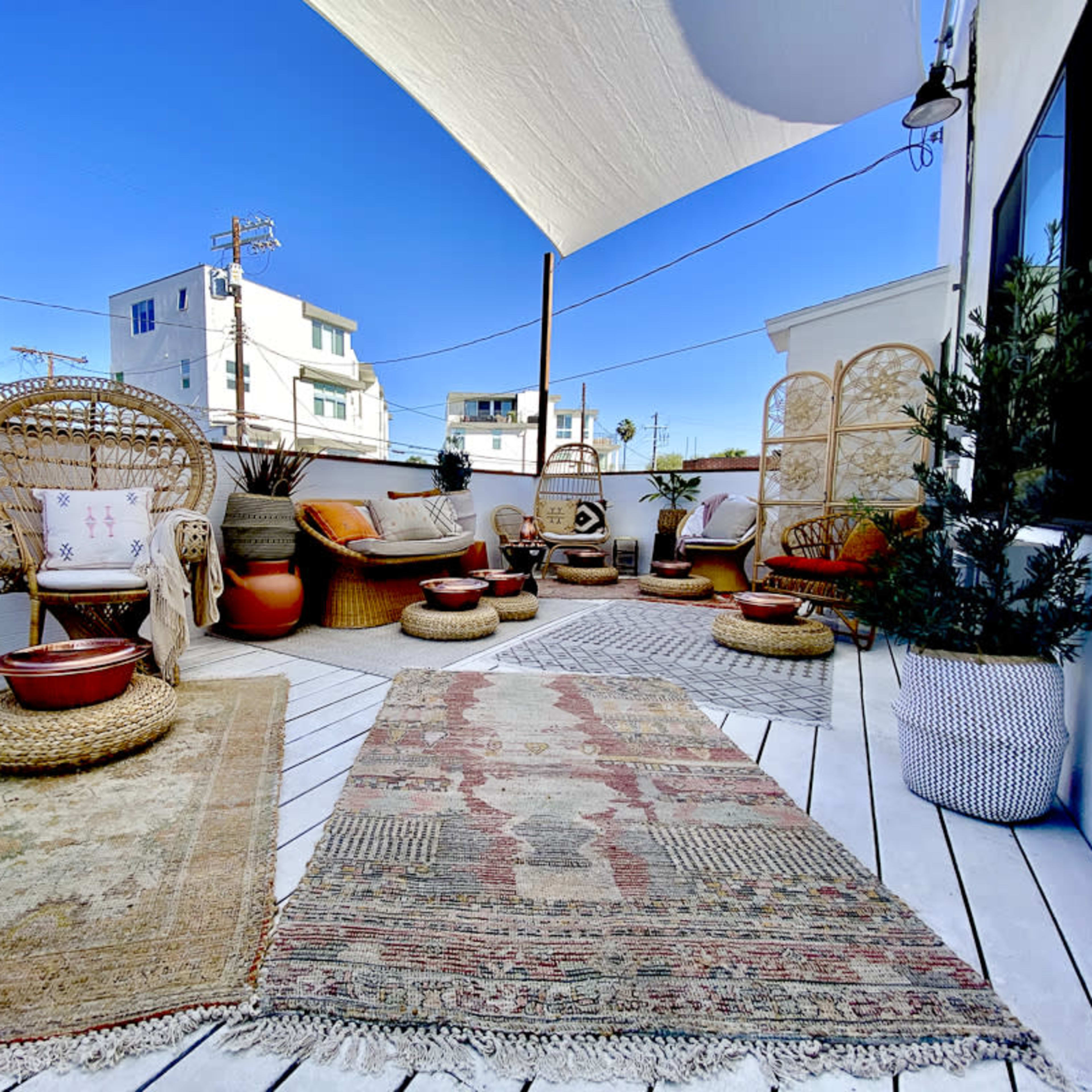 A rooftop terrace adorned with various seating arrangements, decorative rugs, and potted plants under a clear blue sky.