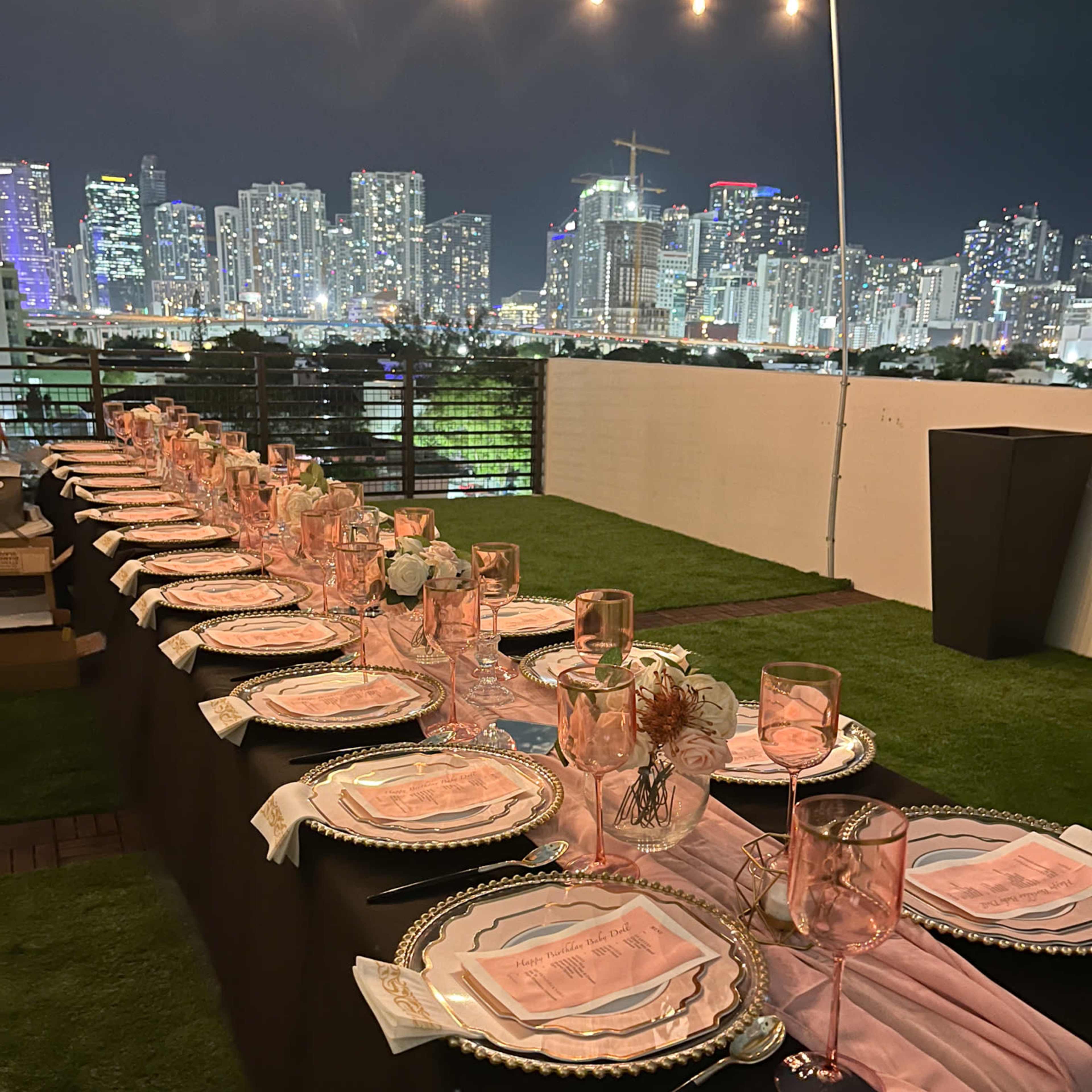 The scene features a large "MARRY ME" display illuminated with lights on a rooftop, surrounded by candles and flowers, with a city skyline in the background.