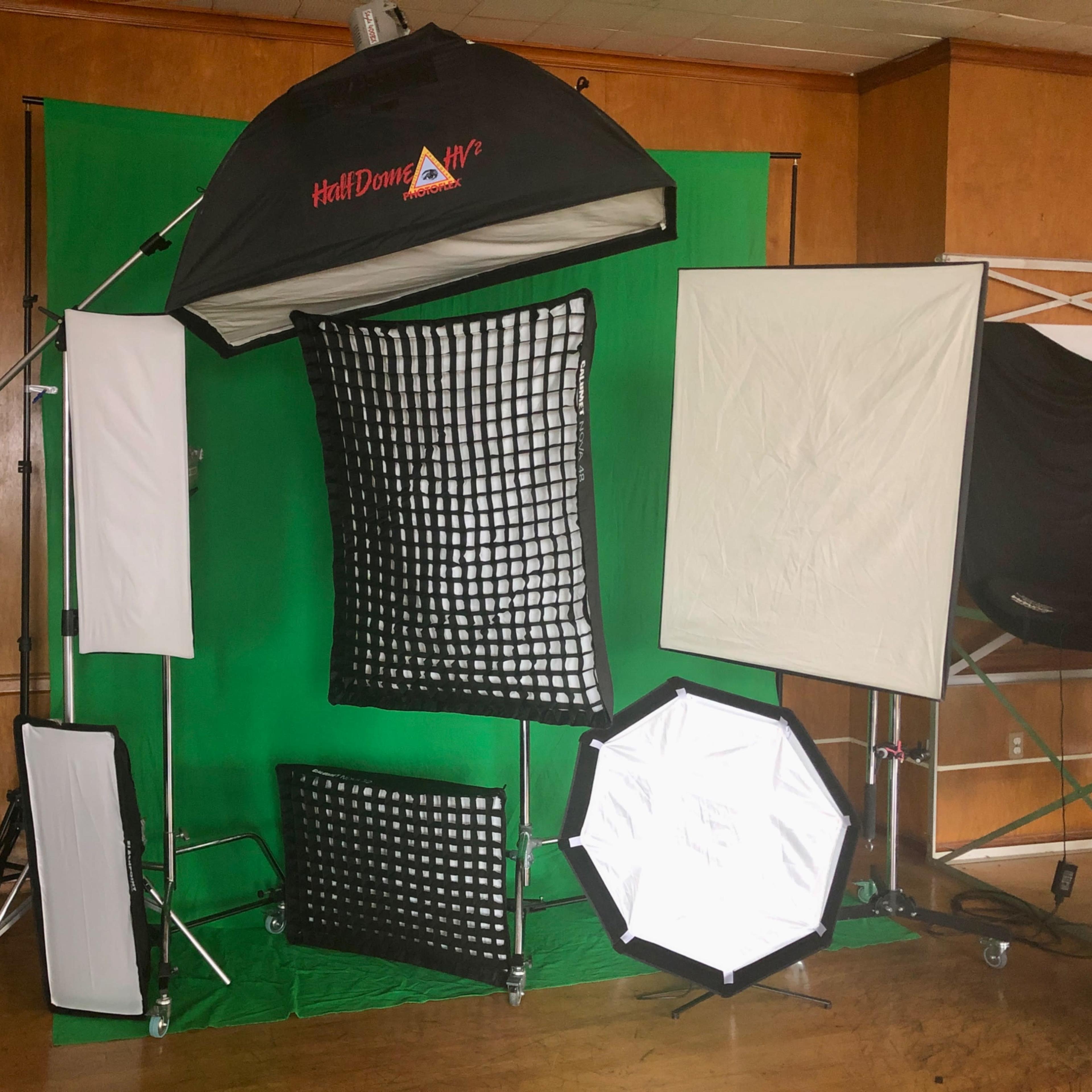 A professional photography setup featuring a green backdrop surrounded by various lighting equipment and softboxes.