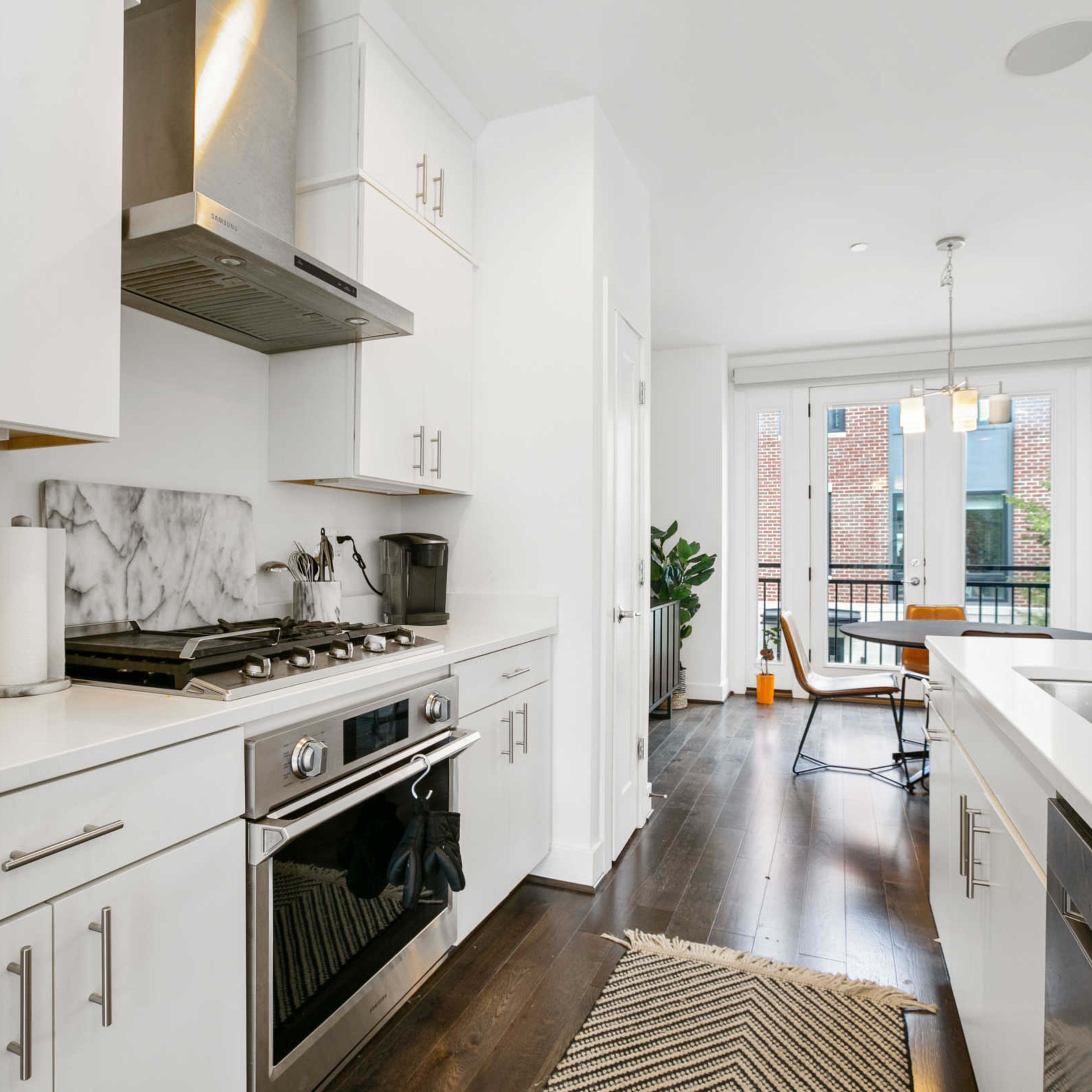 A modern kitchen features white cabinetry, stainless steel appliances, and a marble backsplash, with a view of a balcony through large windows.