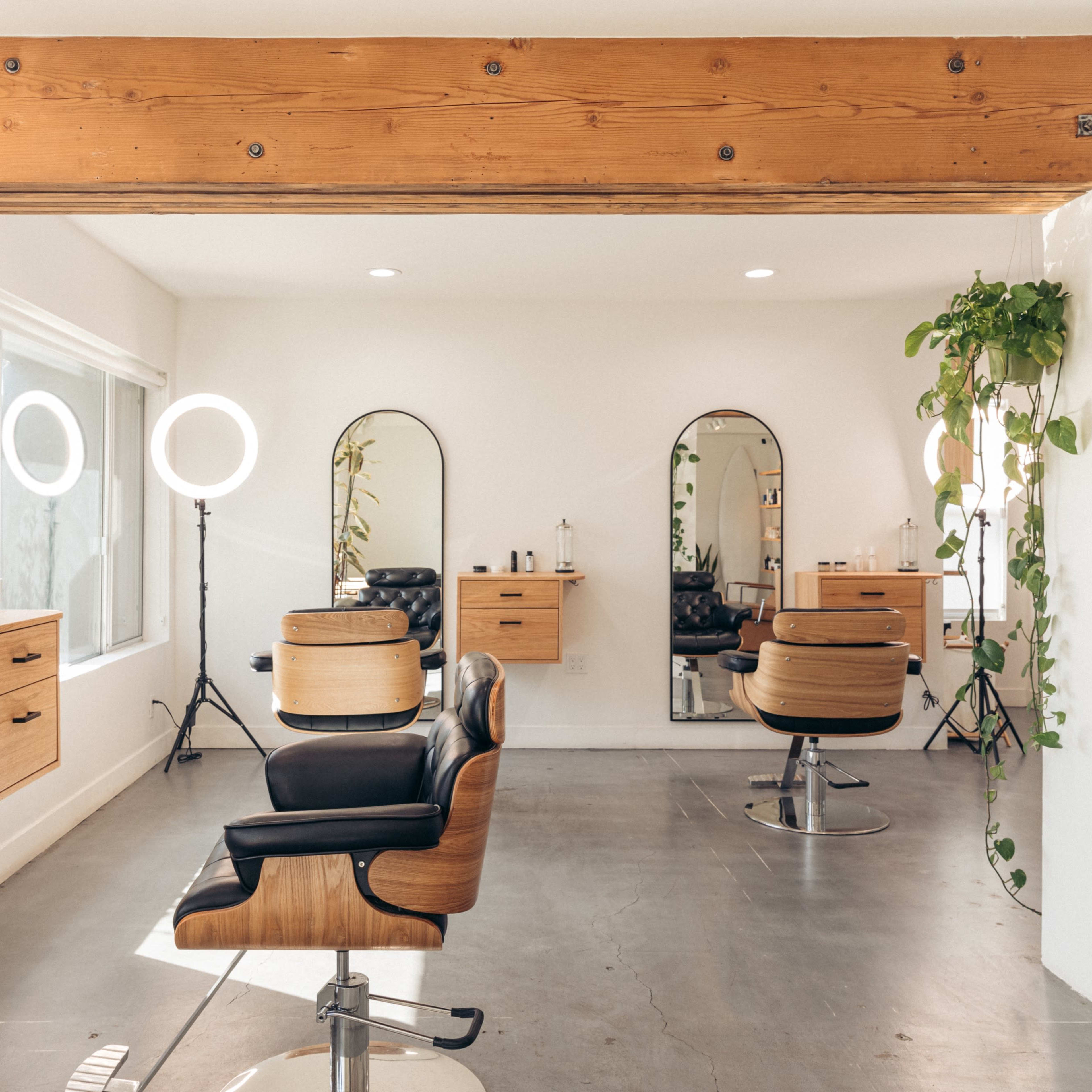 A modern hair salon features sleek styling chairs, wall mirrors, and bright lighting, with greenery accenting the space.