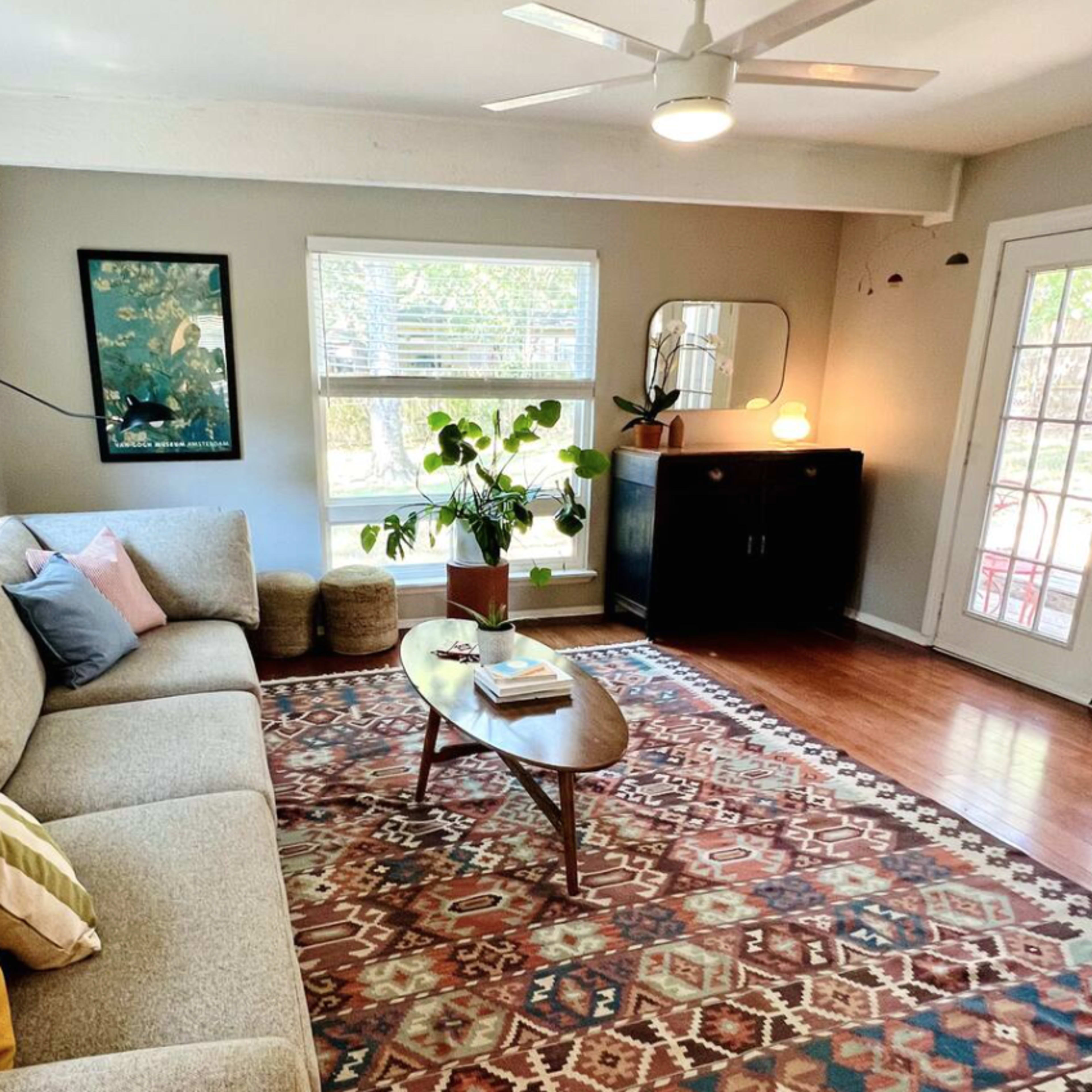 A modern living room features a sofa, a coffee table, a small plant, and large windows that let in natural light.