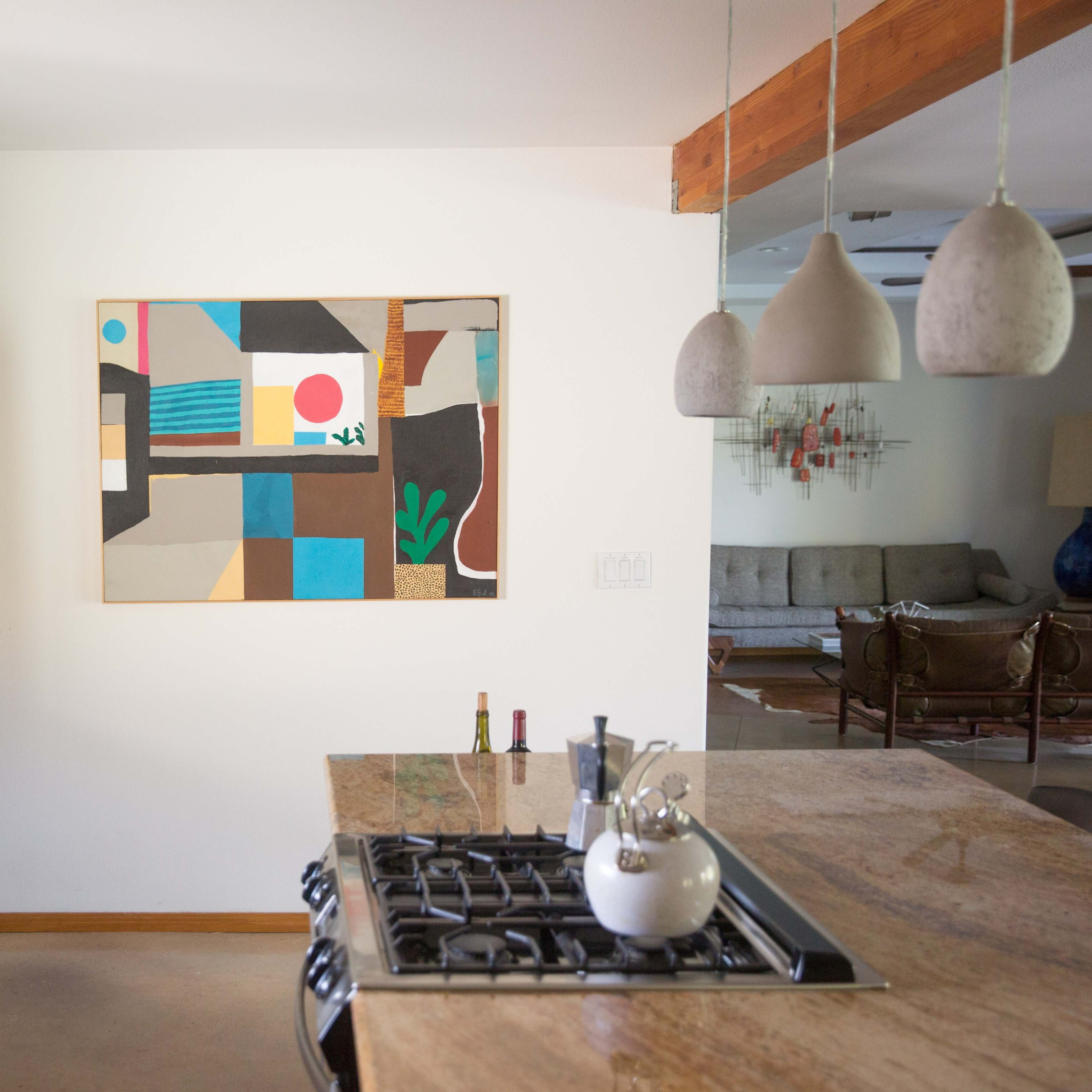 A modern kitchen features wooden cabinetry, a stainless steel refrigerator, and a large abstract painting on the wall.