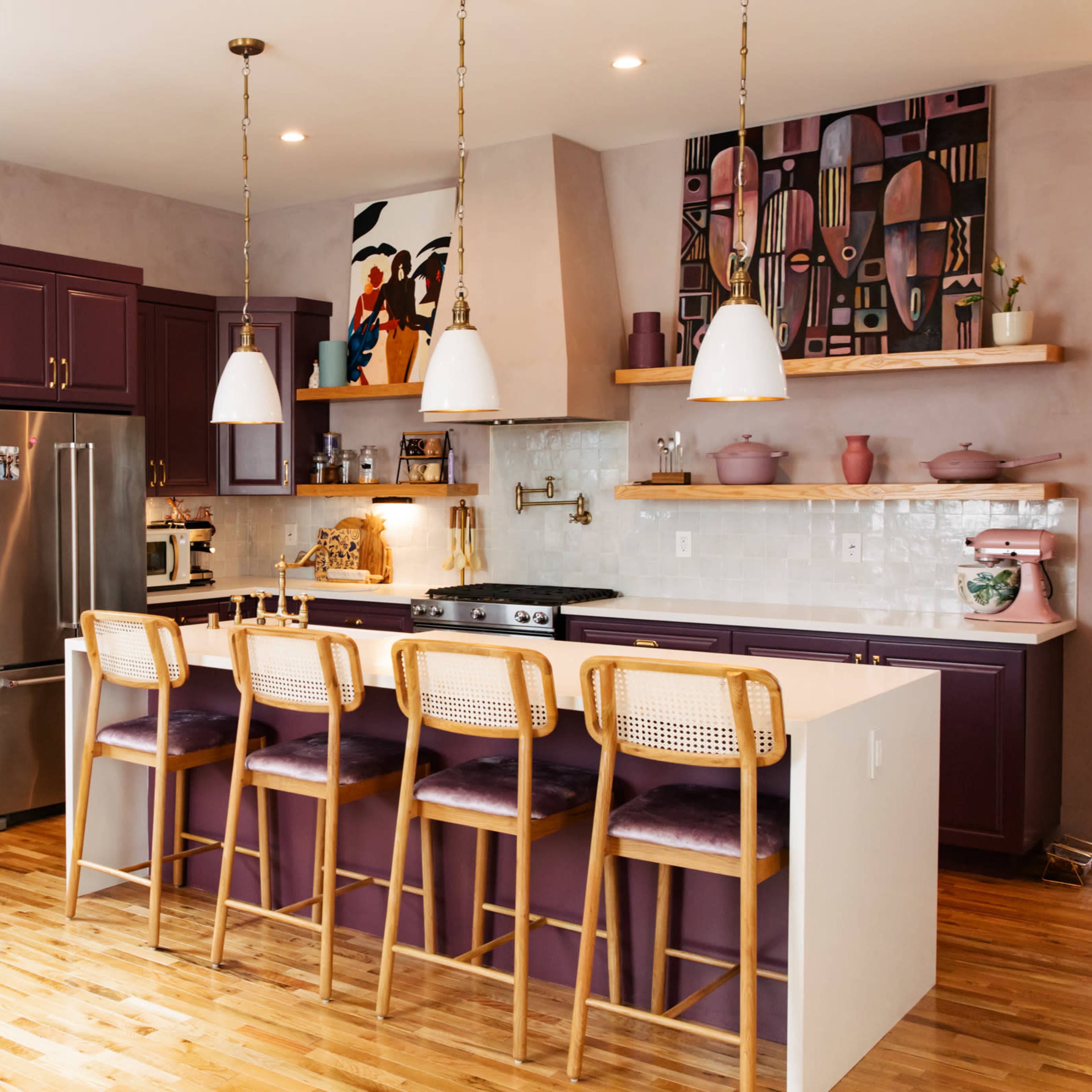 A modern kitchen features purple cabinetry, a spacious island with bar stools, and decorative wall art.