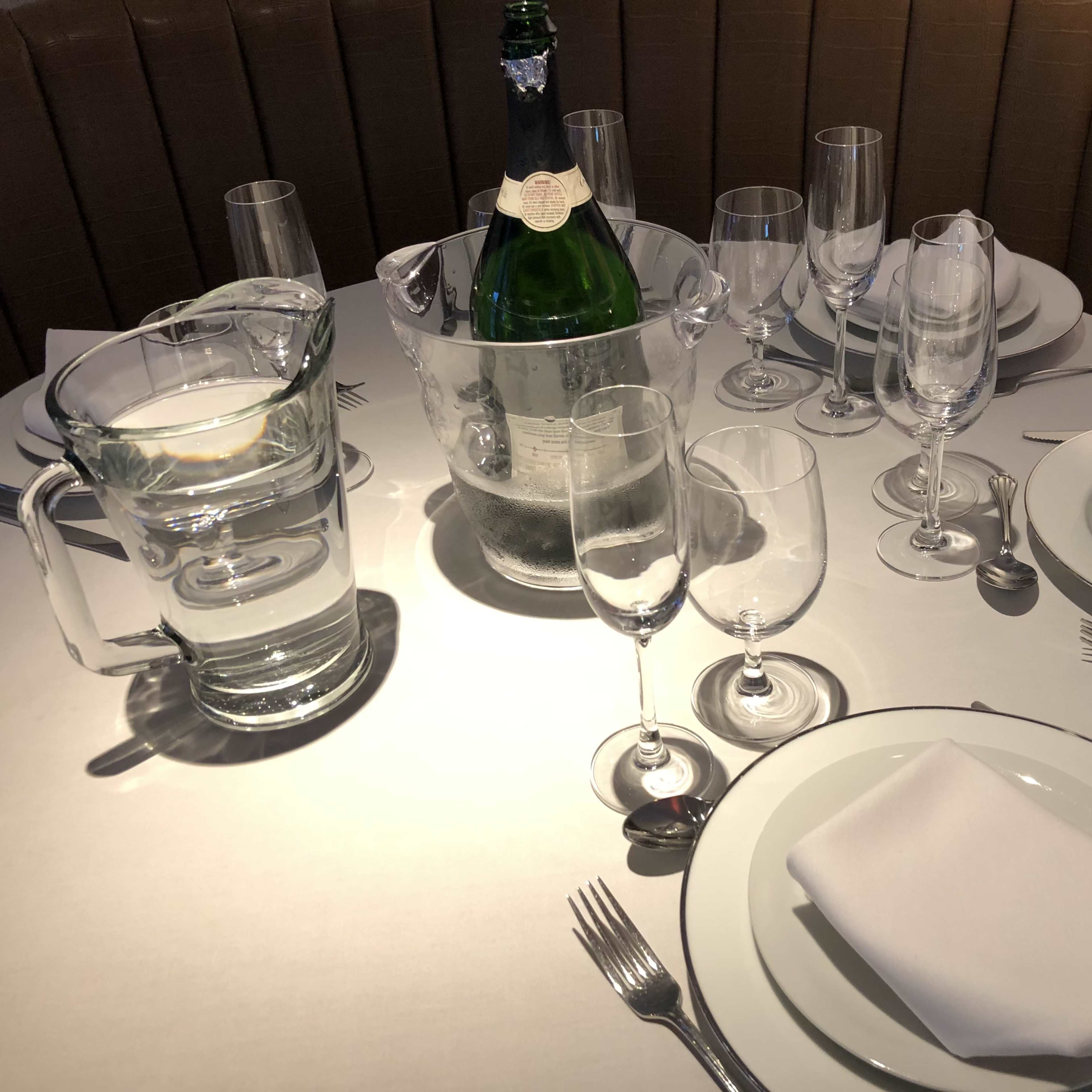 A dining table is set with multiple glassware, a bottle of champagne in an ice bucket, and neatly arranged plates and utensils.