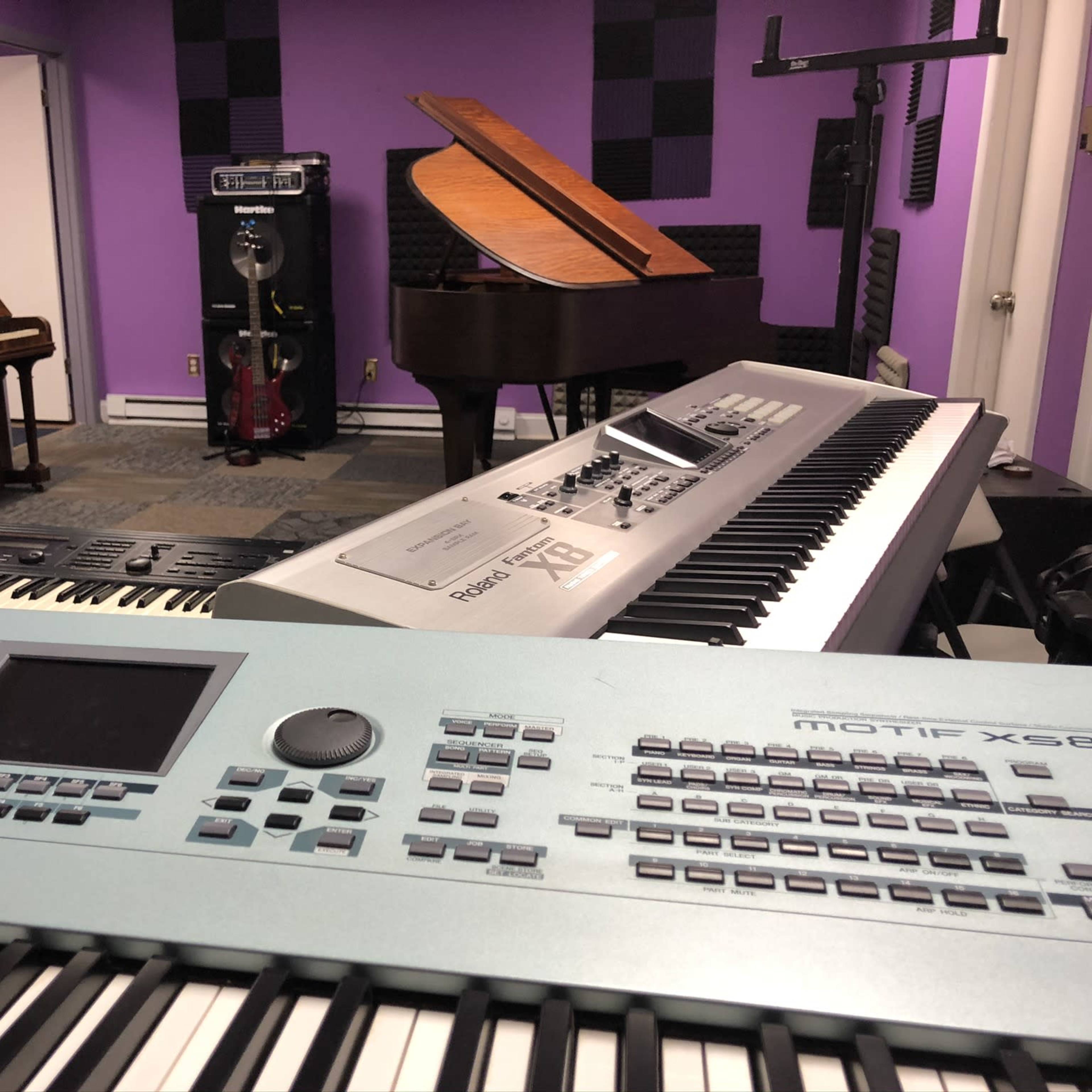 A music studio with various instruments, including a grand piano, an upright piano, and multiple keyboards, set against purple walls.