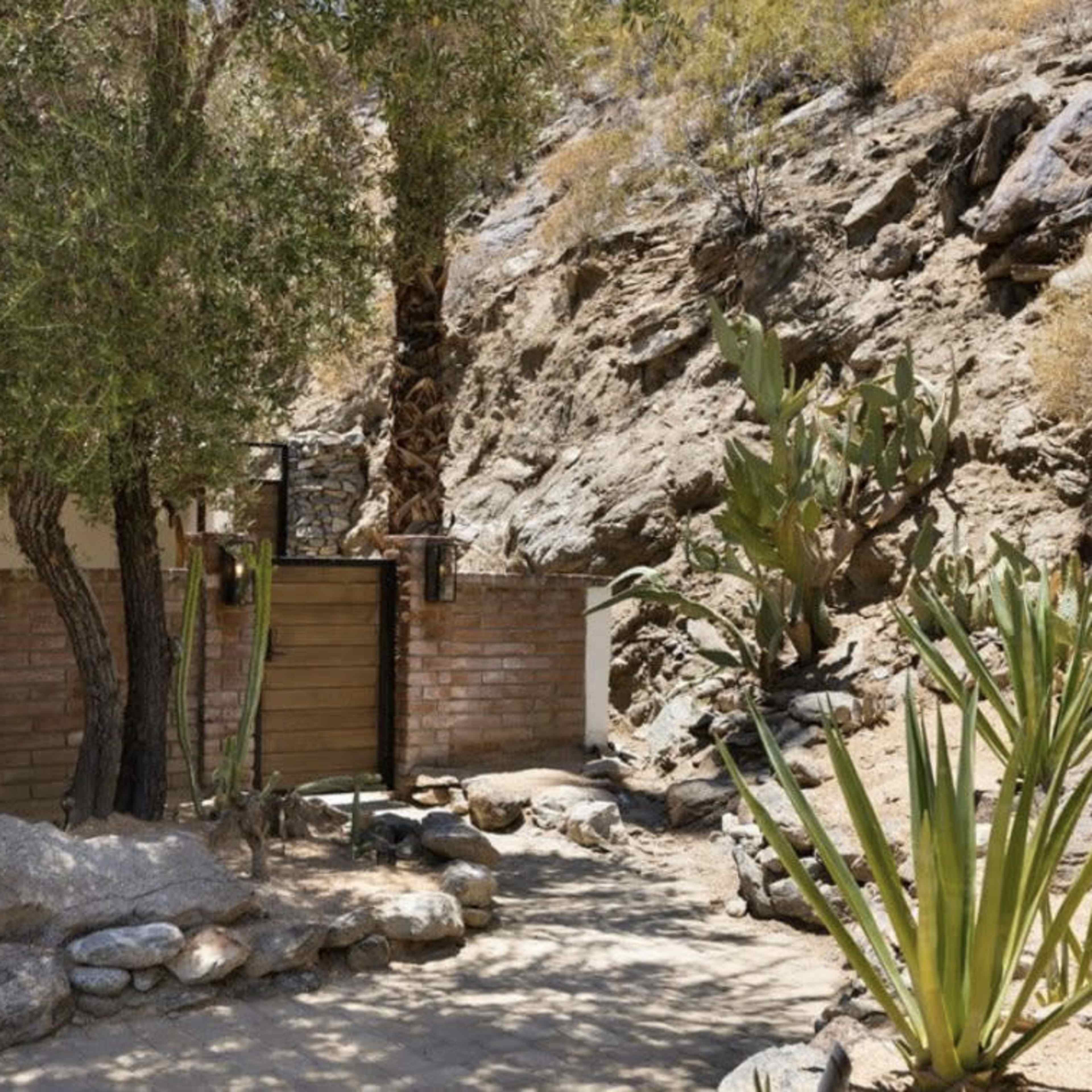 A landscaped area featuring a stone path, a wooden door, and plants beside a rocky hillside.