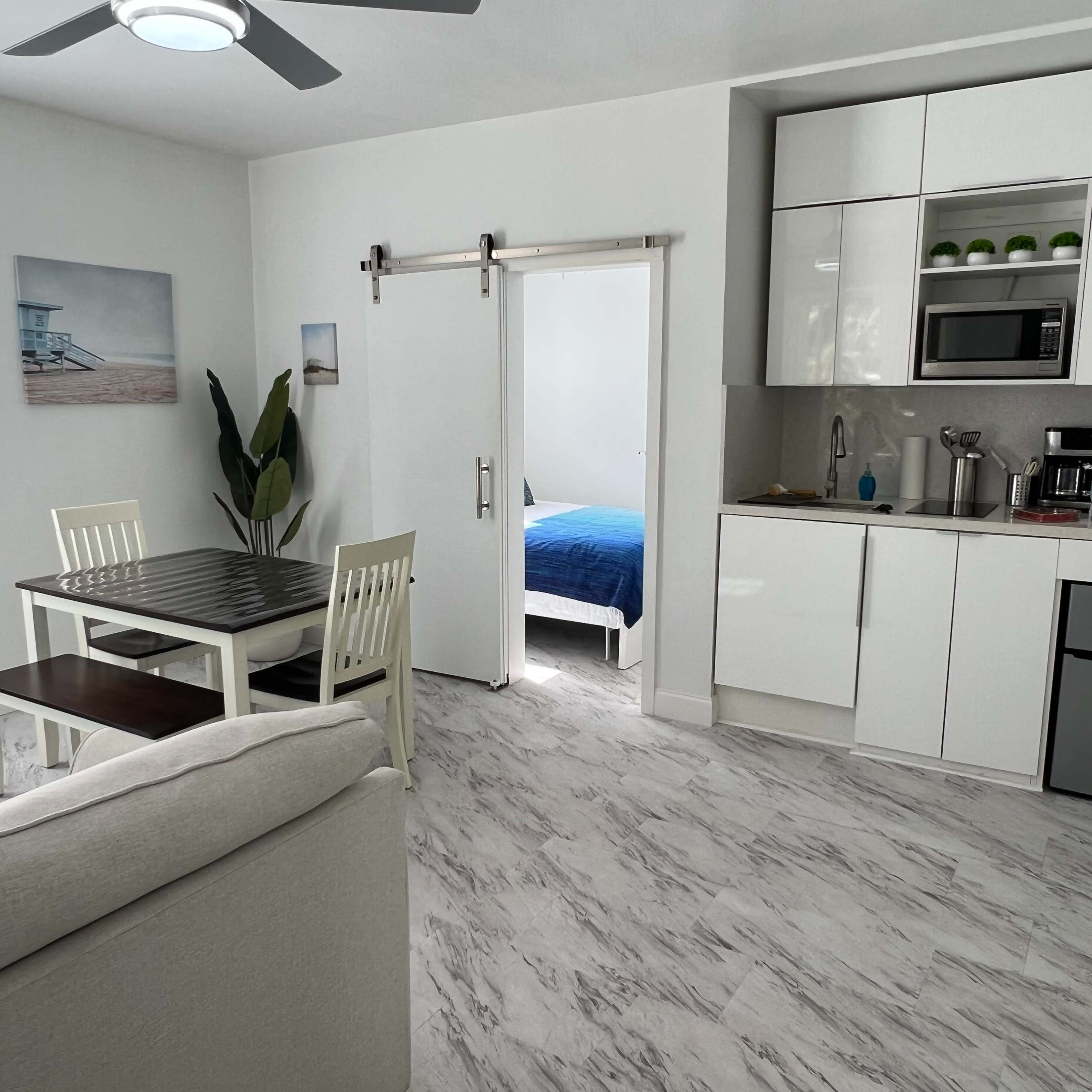A modern, open-concept living space featuring a dining area, kitchenette, and a door leading to a bedroom.