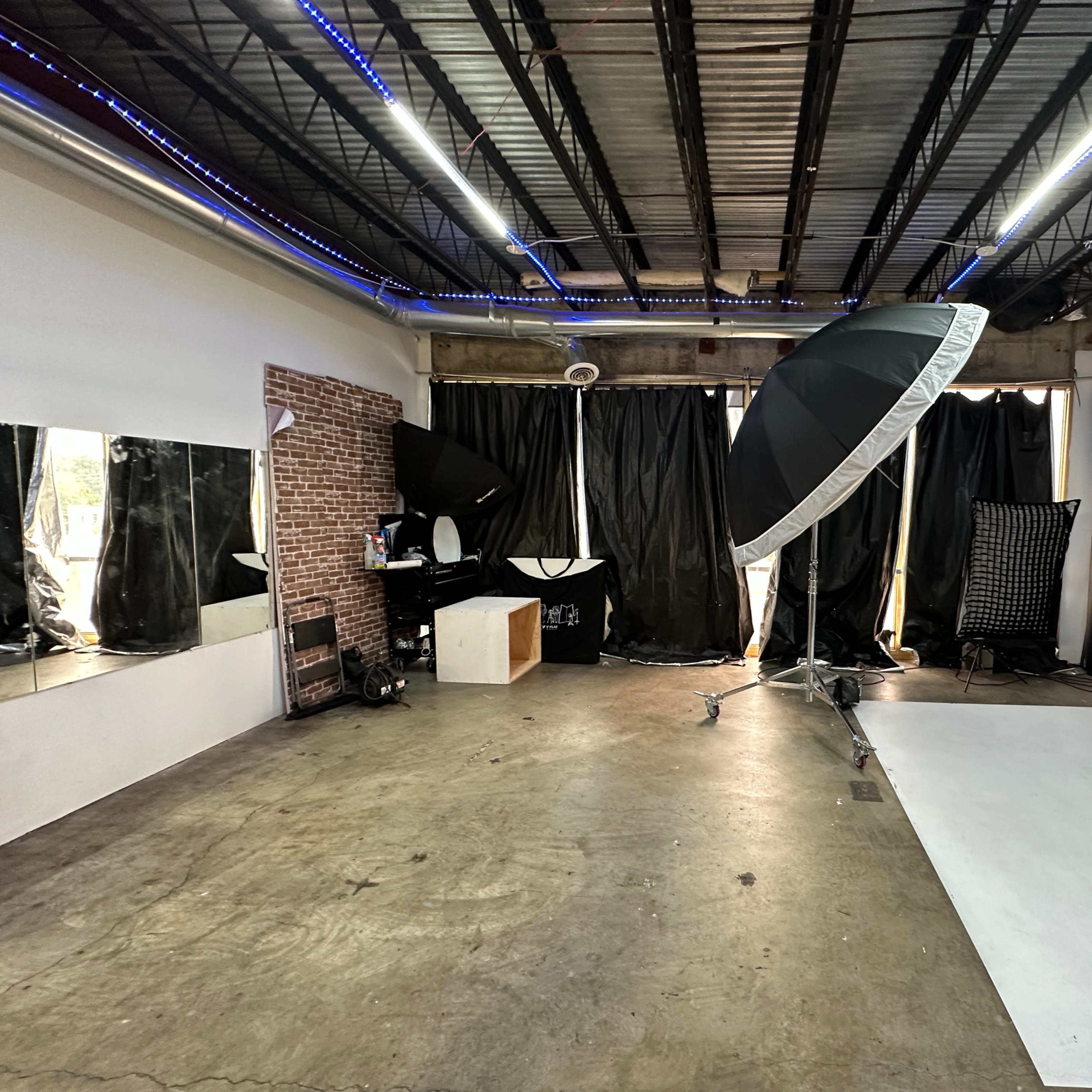 A photography studio featuring a white backdrop, large softbox light, mirrors, and black curtains.