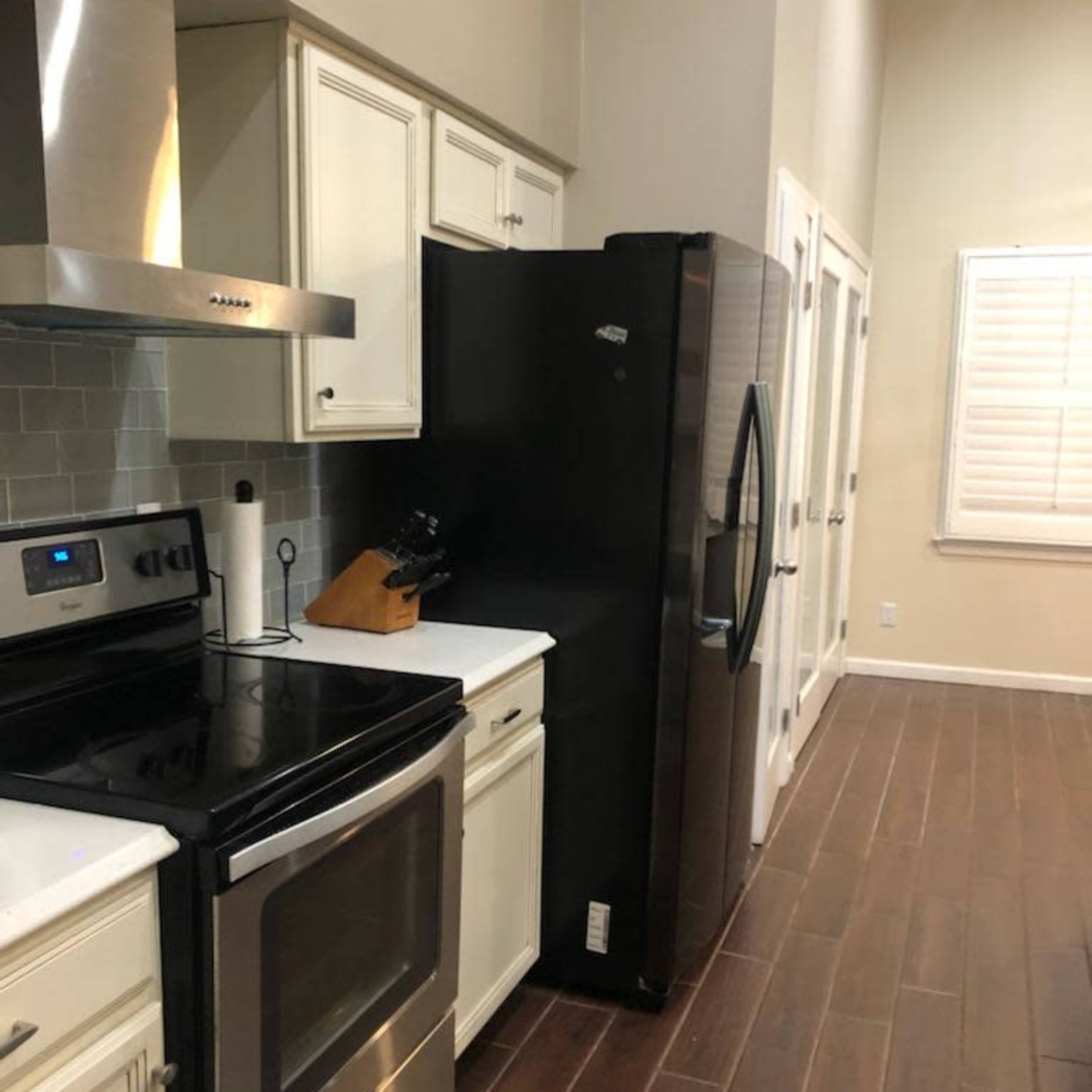 A modern kitchen with stainless steel appliances, including an oven and a refrigerator, along a wooden floor with beige walls.