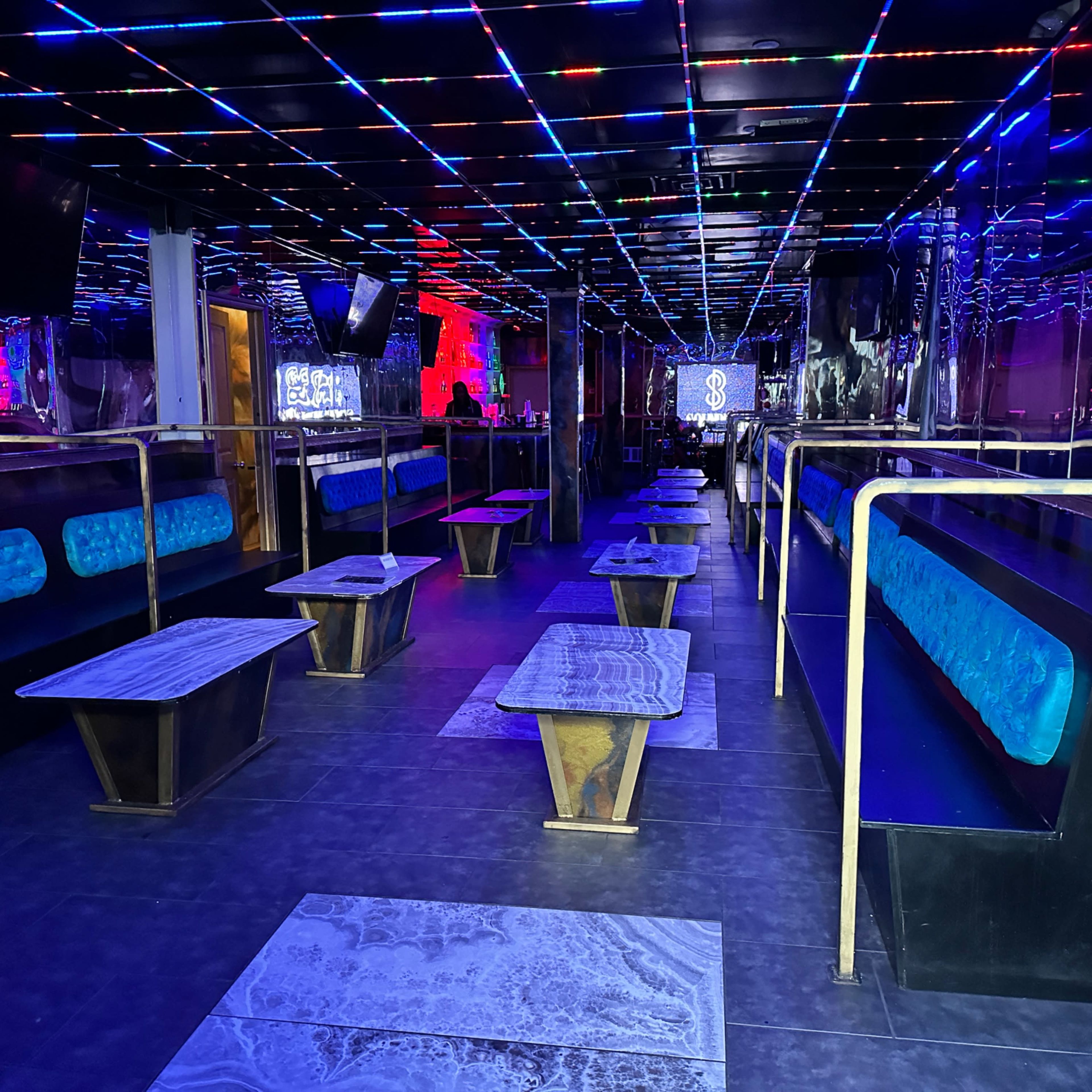 The interior of a nightclub featuring rows of seating and tables under colorful LED lights.