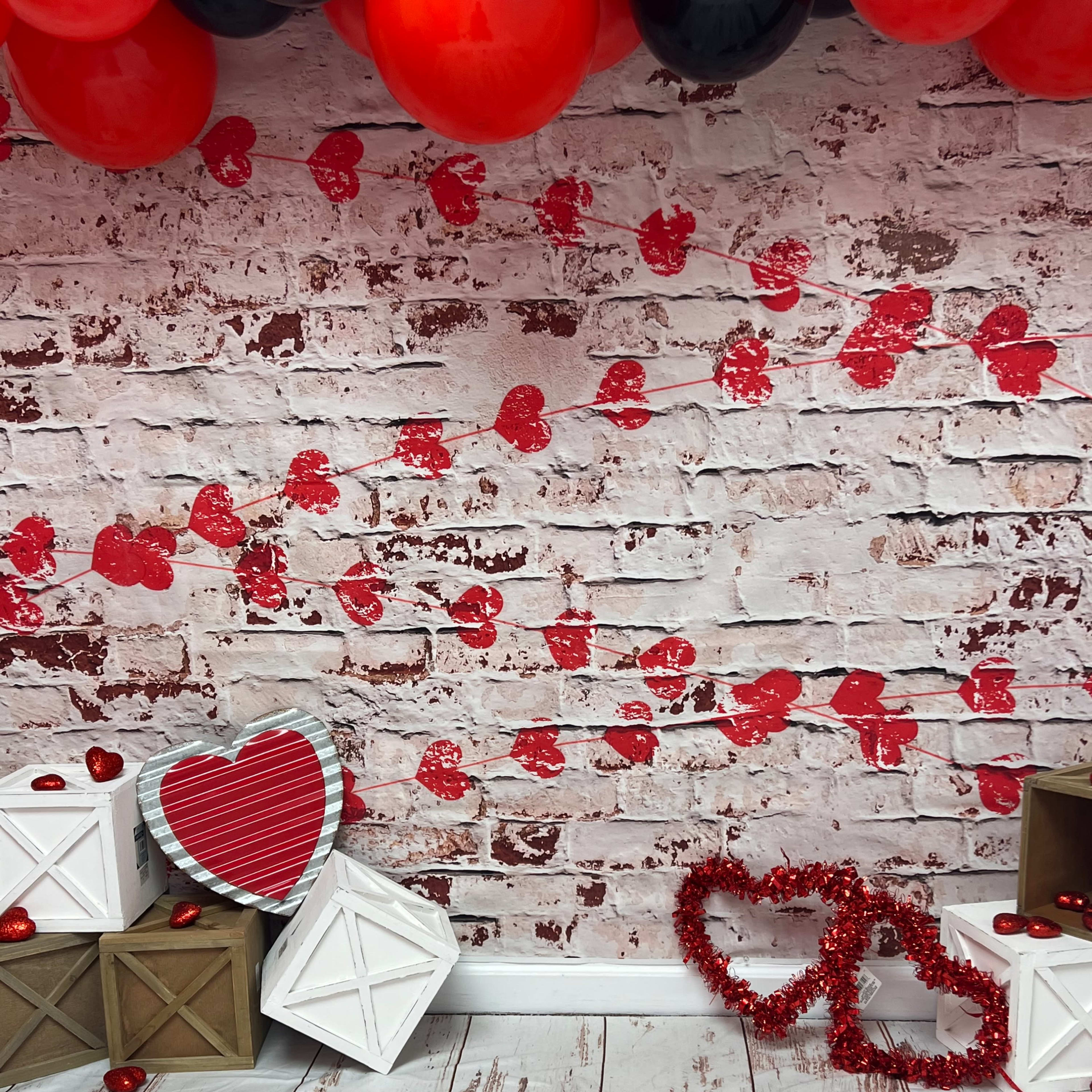 The scene features a backdrop of a brick wall decorated with red heart cutouts, alongside wooden boxes and a couple of heart-shaped decorations.