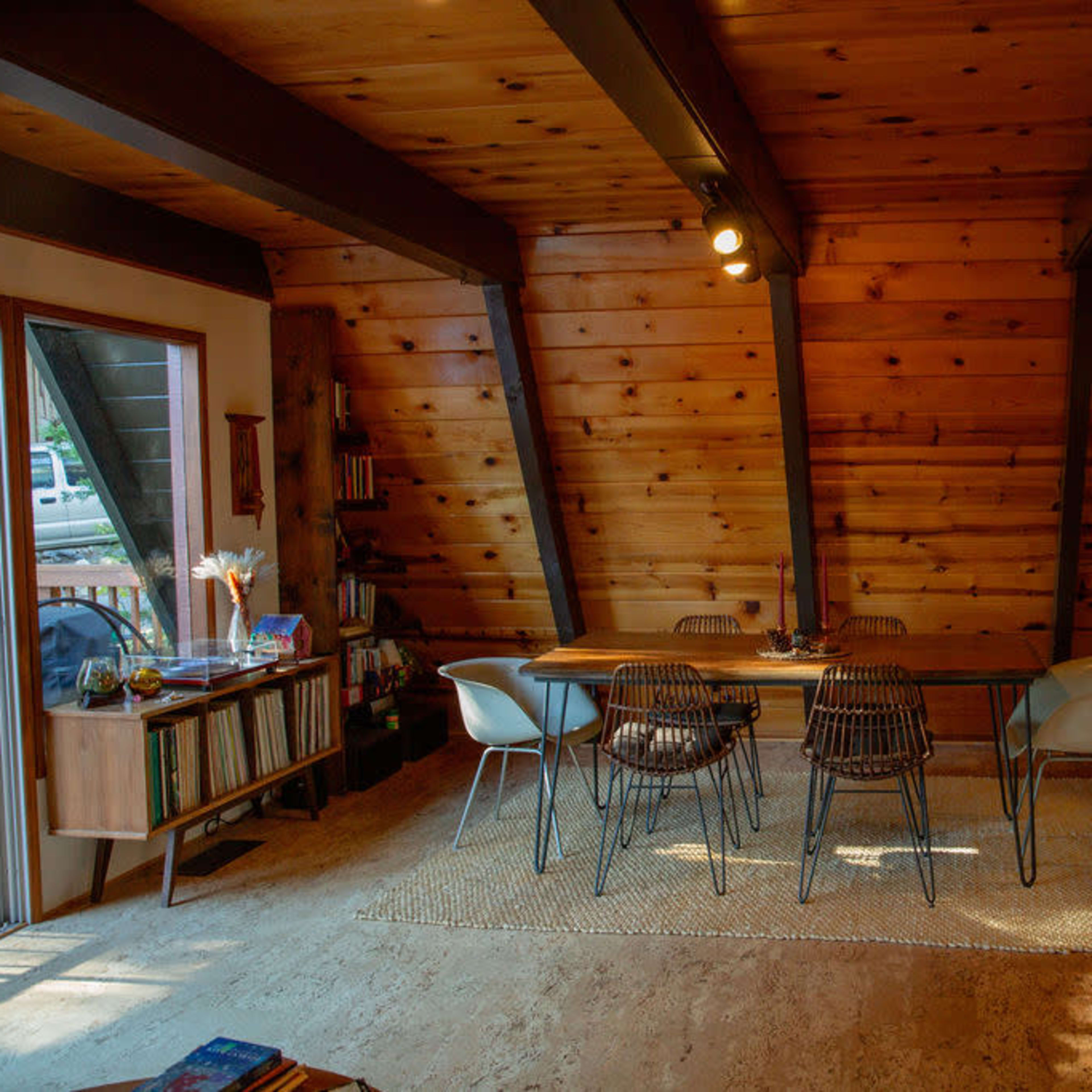 A dining area with a wooden table and chairs beneath sloped wooden beams, adjacent to a kitchen with wooden cabinetry.