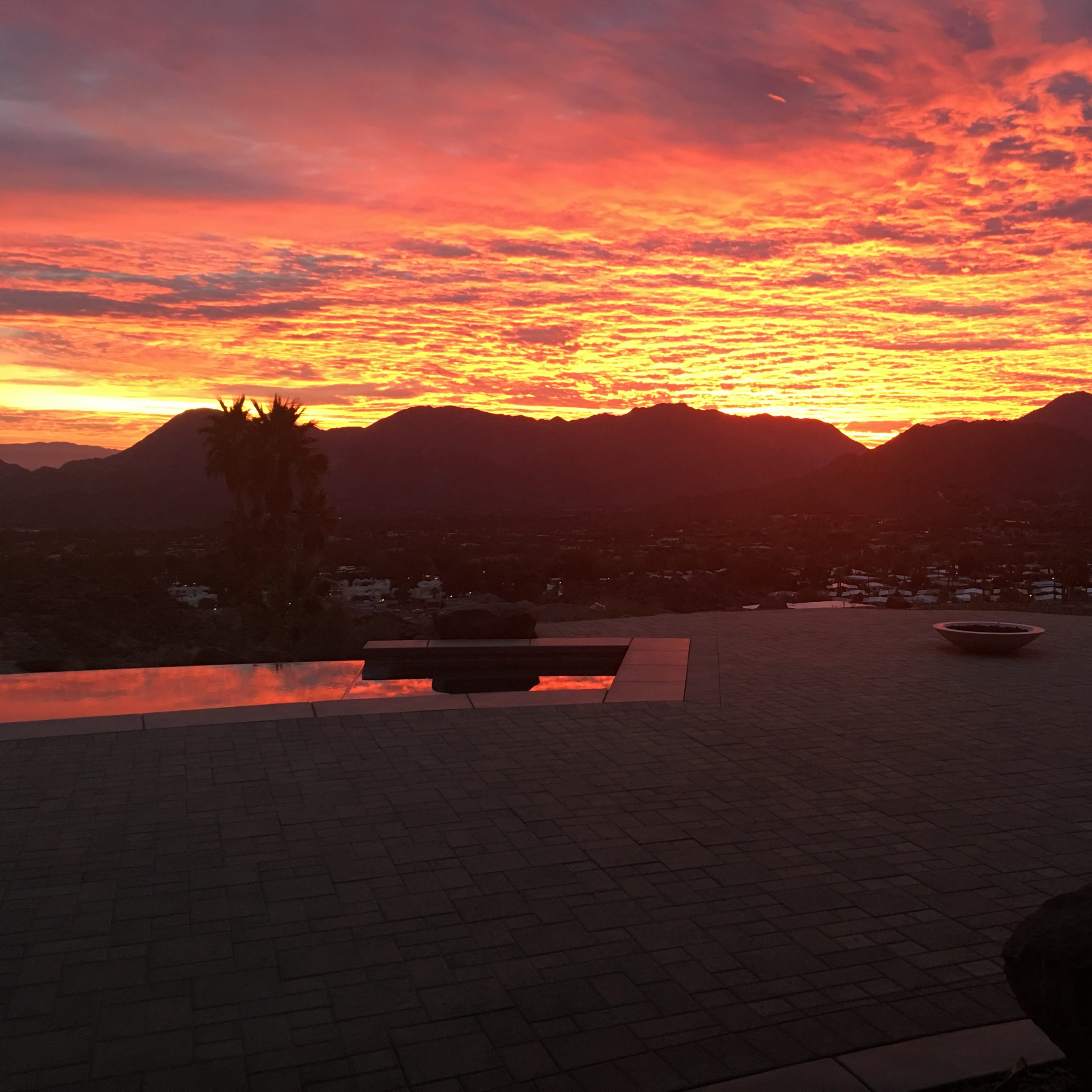 A vibrant sunset over mountains, with a reflection on a landscaped patio.