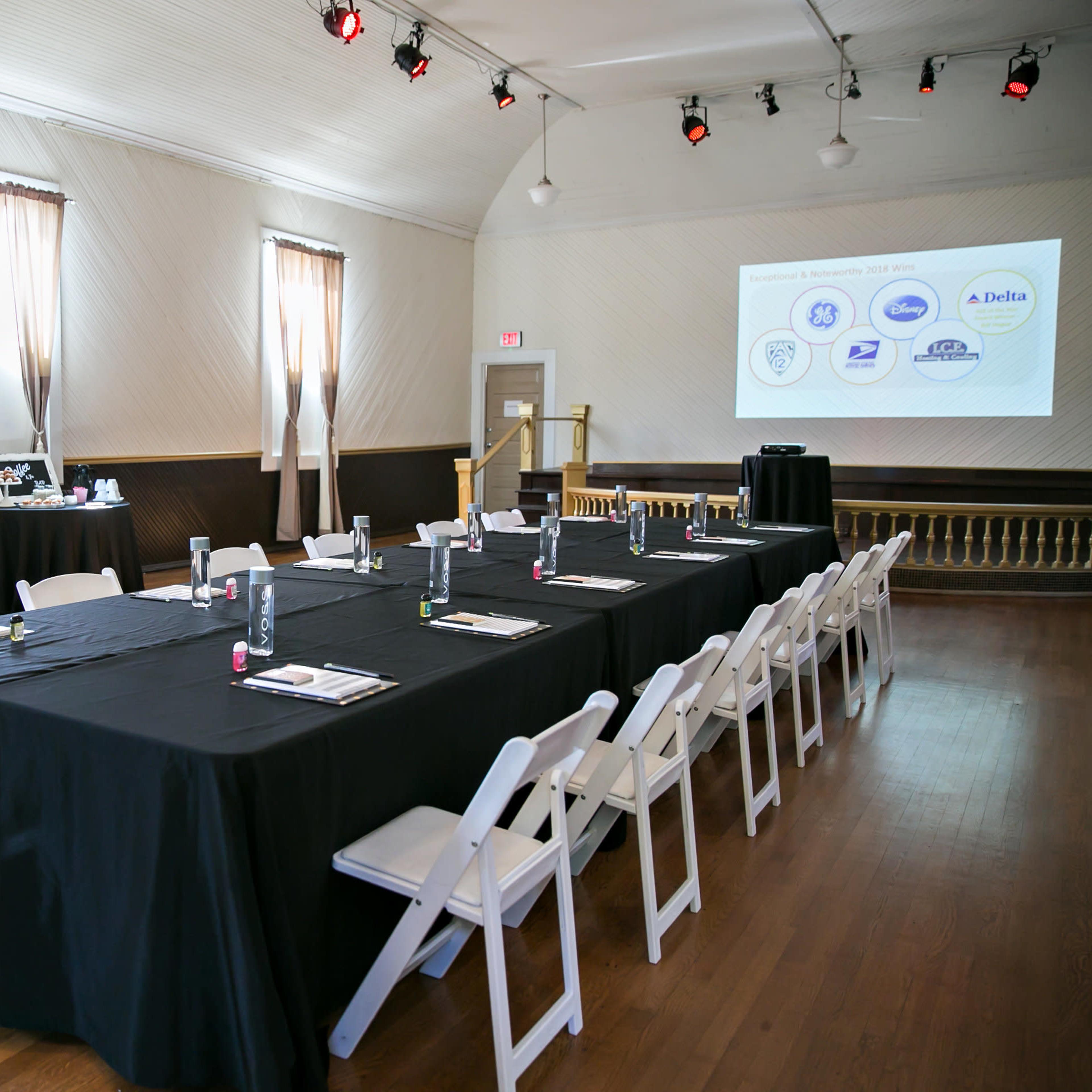 A conference room is set up with black tablecloths covering long tables and a projector screen displaying logos at one end.