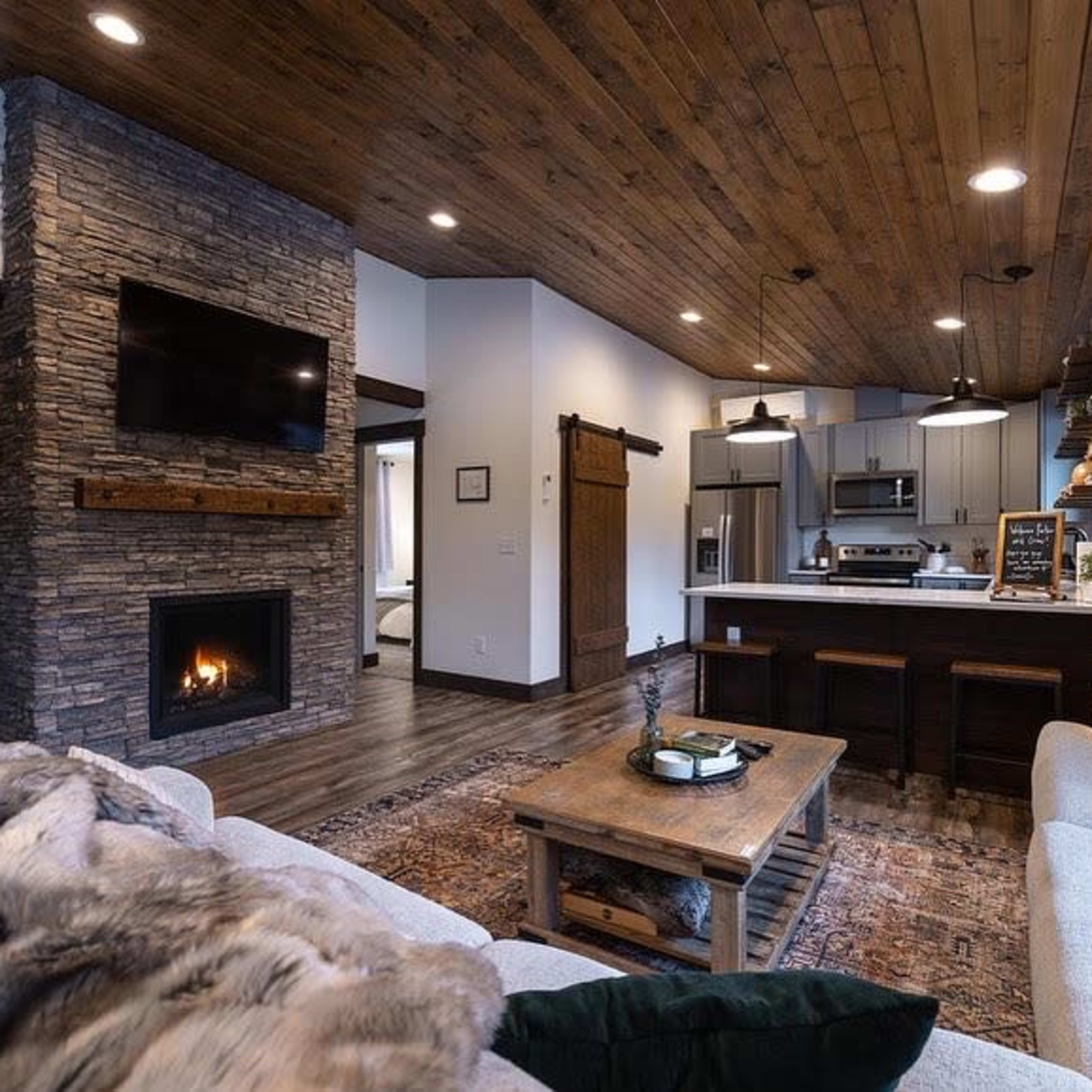 A modern living room with a stone fireplace, wooden ceiling beams, and a cozy seating area featuring a sofa and wooden coffee table.