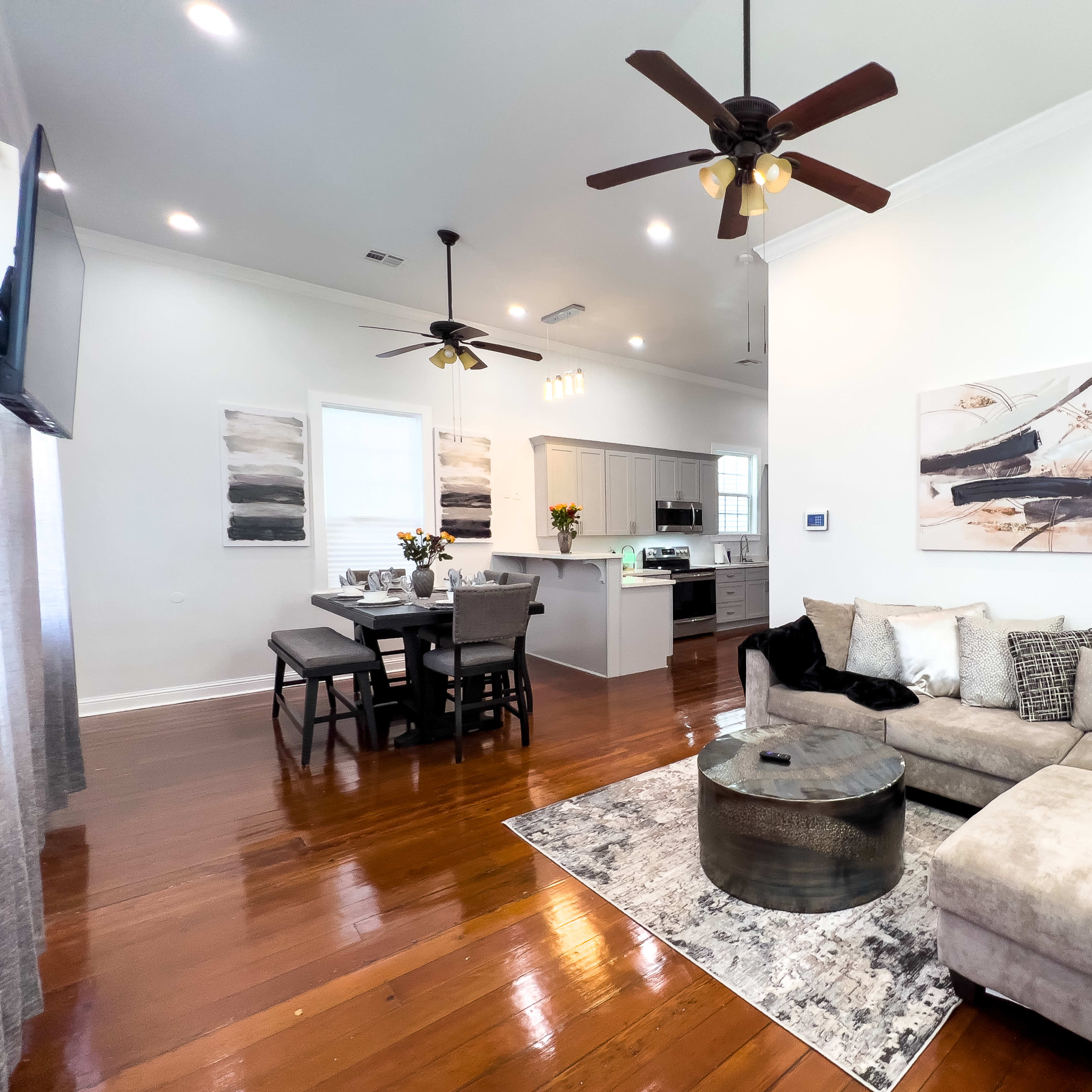 A modern living room and dining area with hardwood floors, featuring a sectional couch, a circular coffee table, and a dining table set for four.