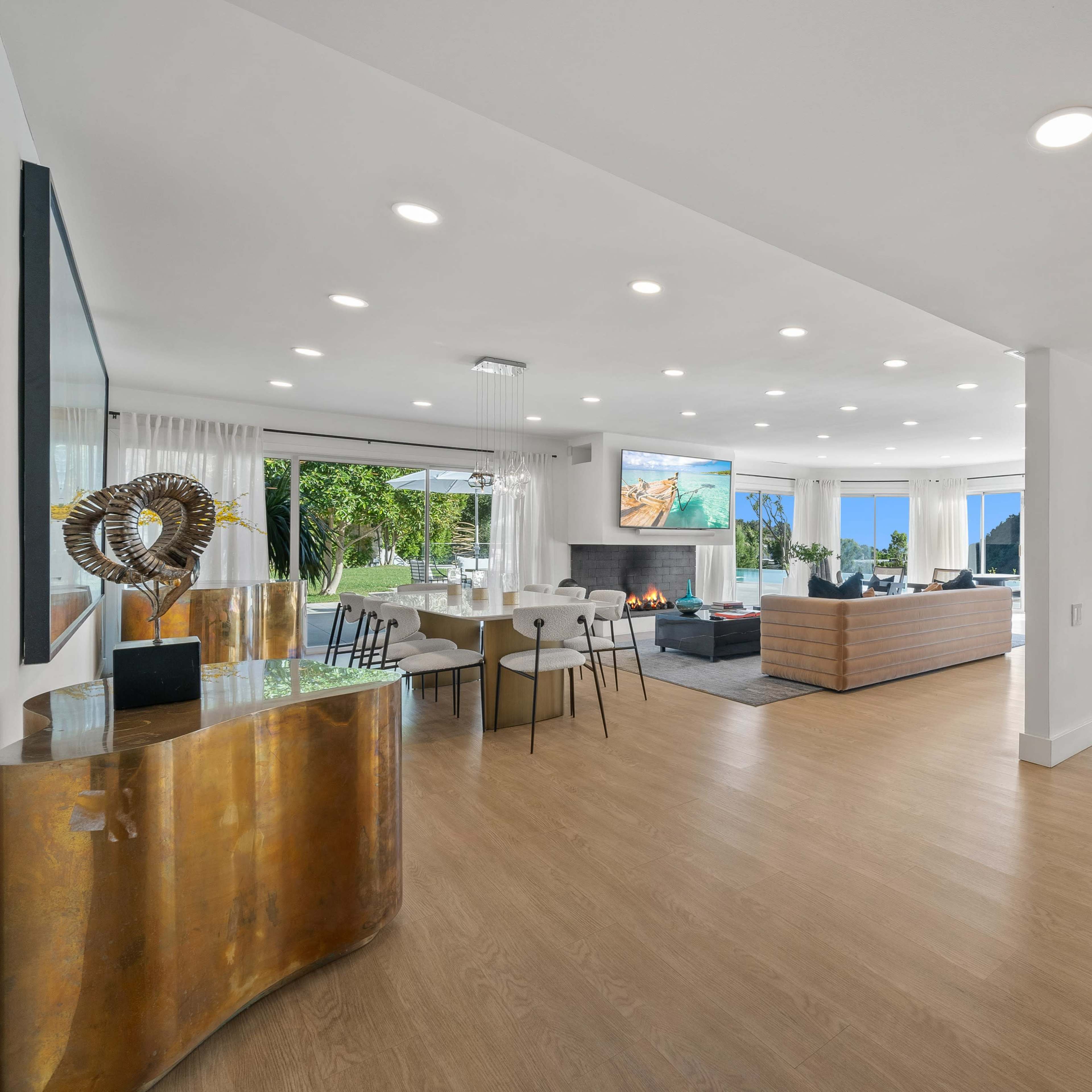 A modern, open-concept living space featuring a mix of dining and lounging areas with large windows that provide natural light and views of the outdoors.