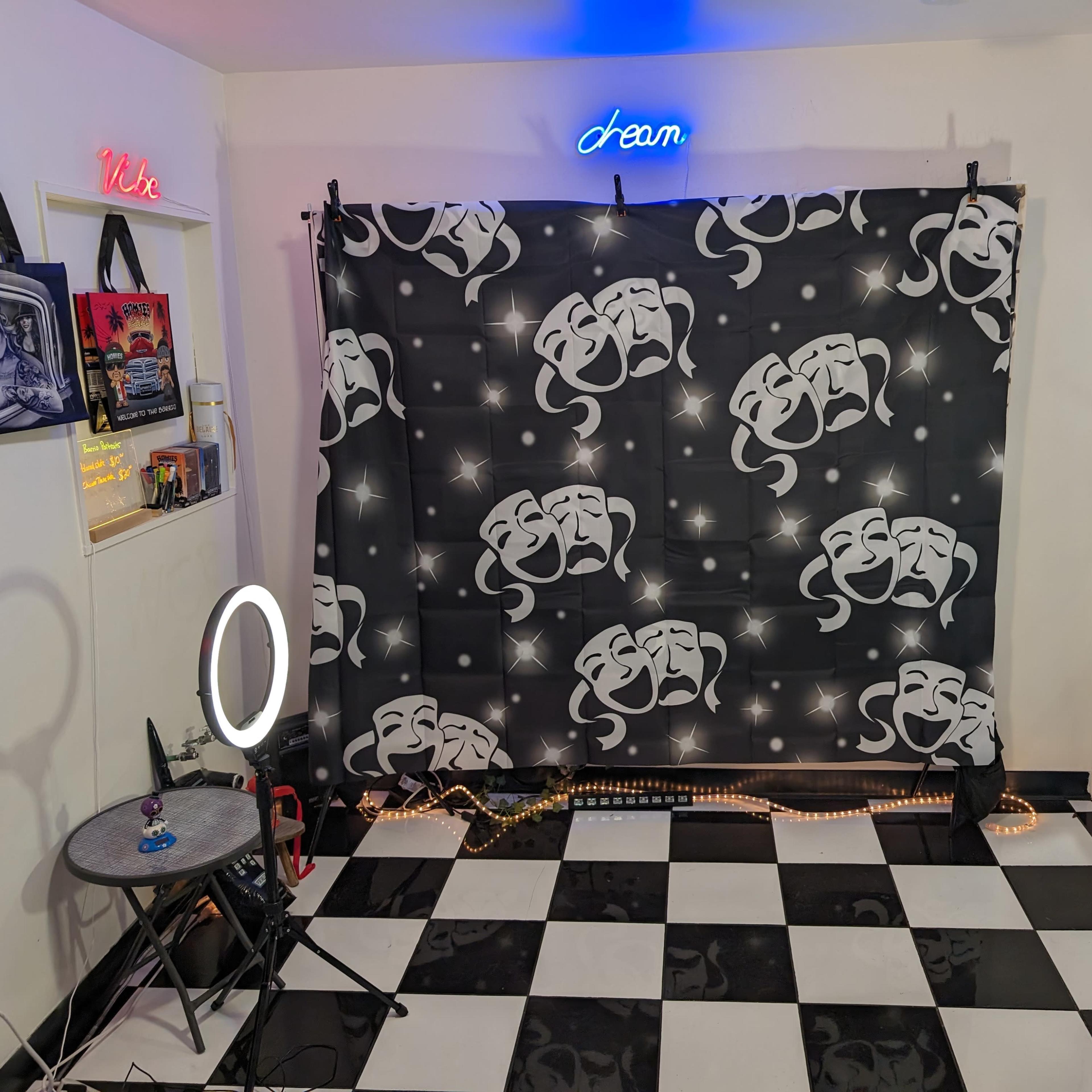 A small room with a black and white checkered floor, featuring a backdrop with theater masks, a circular light, and a table.