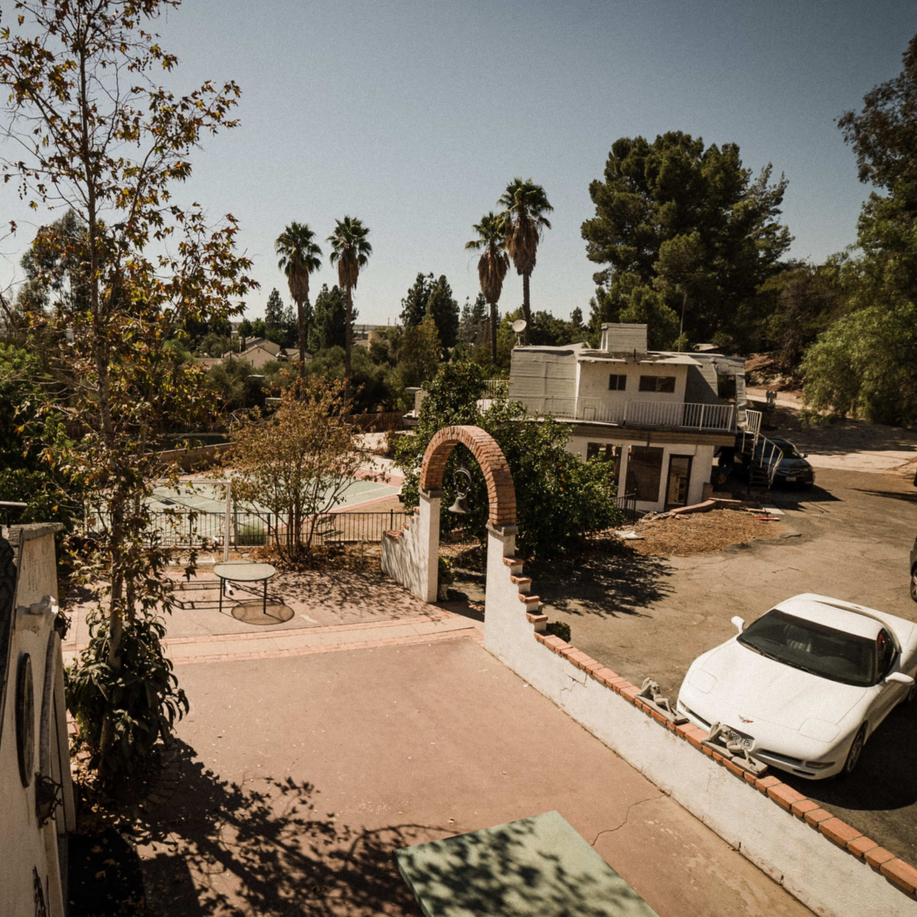A residential area with a white car parked in the foreground and a building with a tower and a weather vane in the background.
