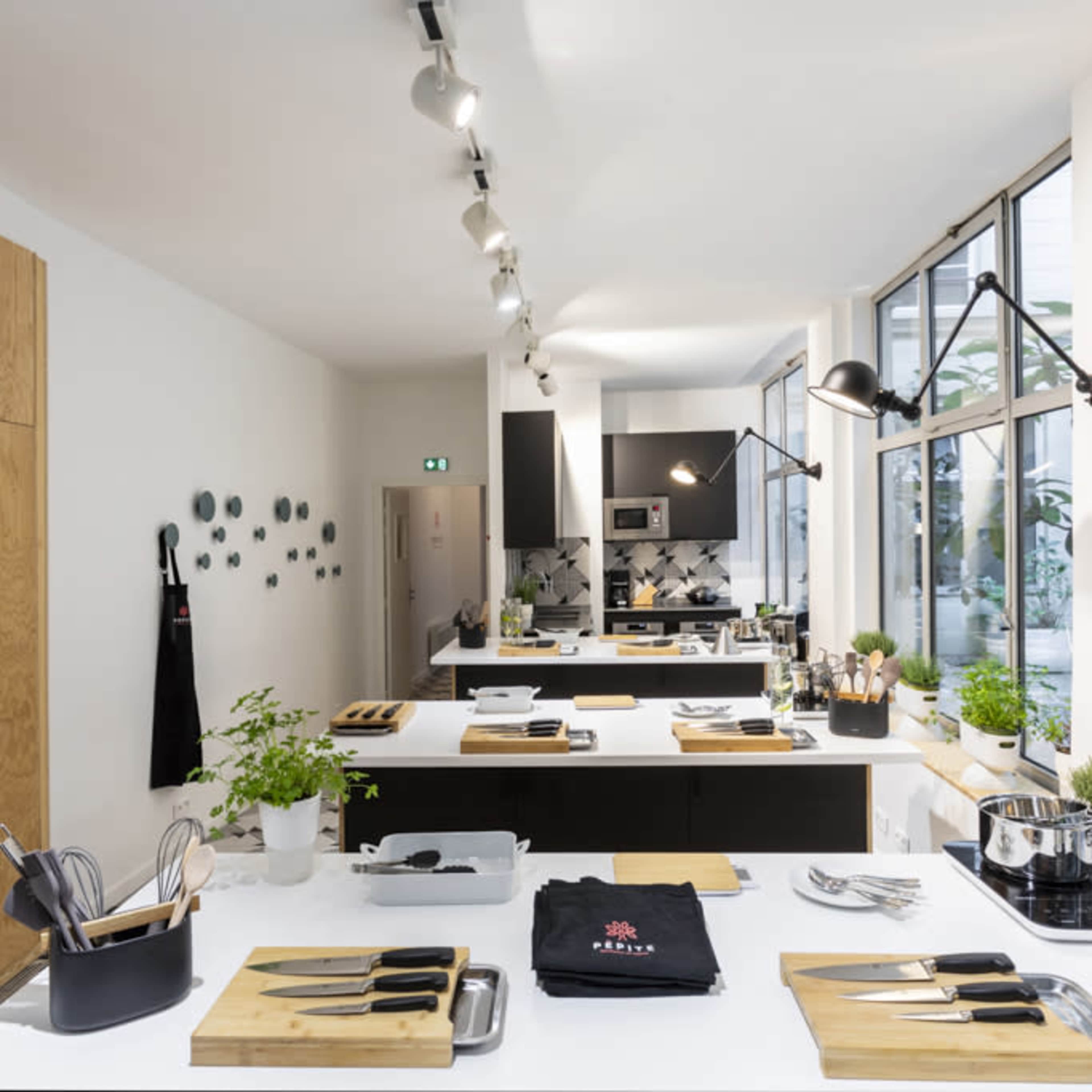 A modern kitchen with wooden cabinetry and multiple cooking stations equipped with utensils, knives, and potted plants.