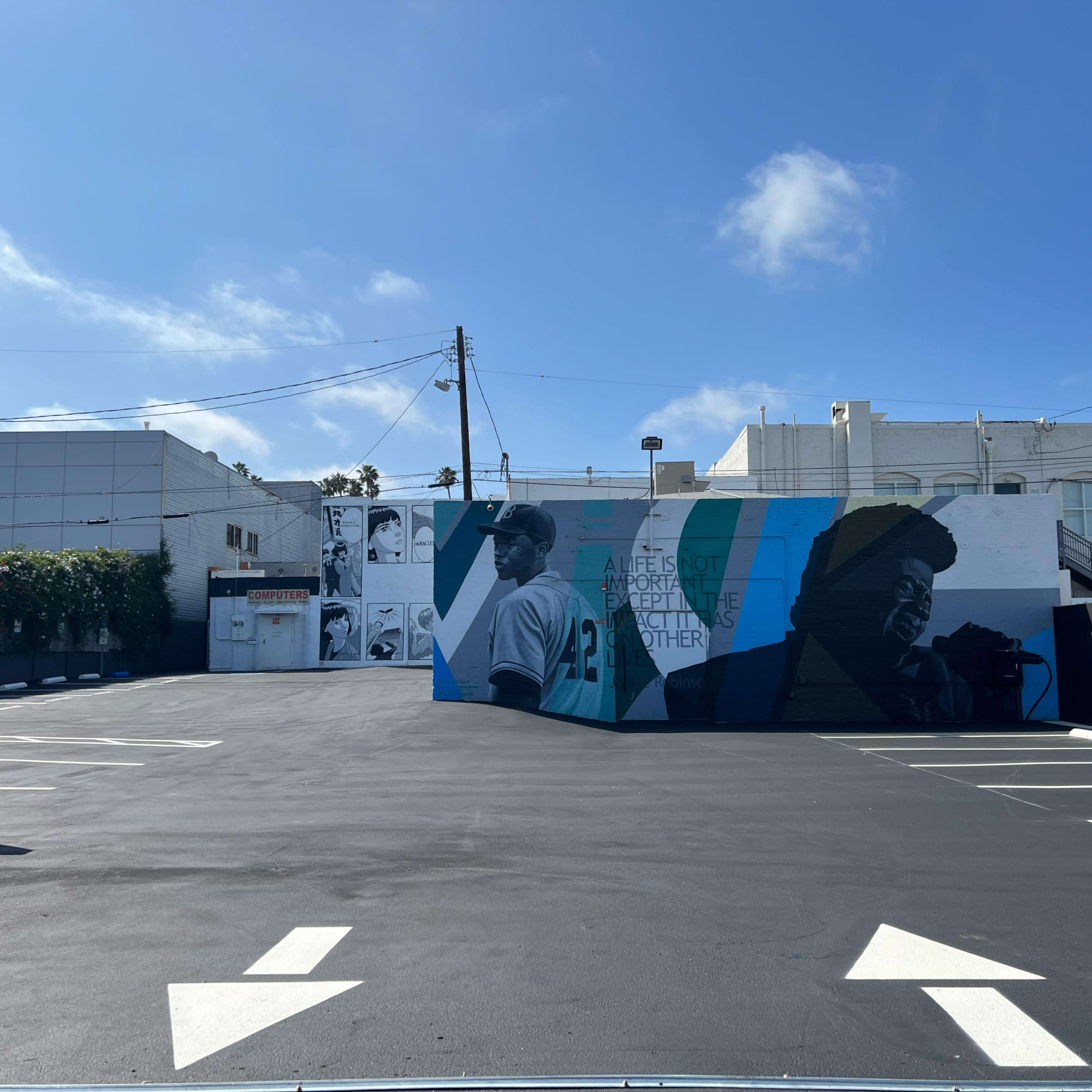 A parking lot with a large mural on the wall depicting two figures against a backdrop of blue and green.
