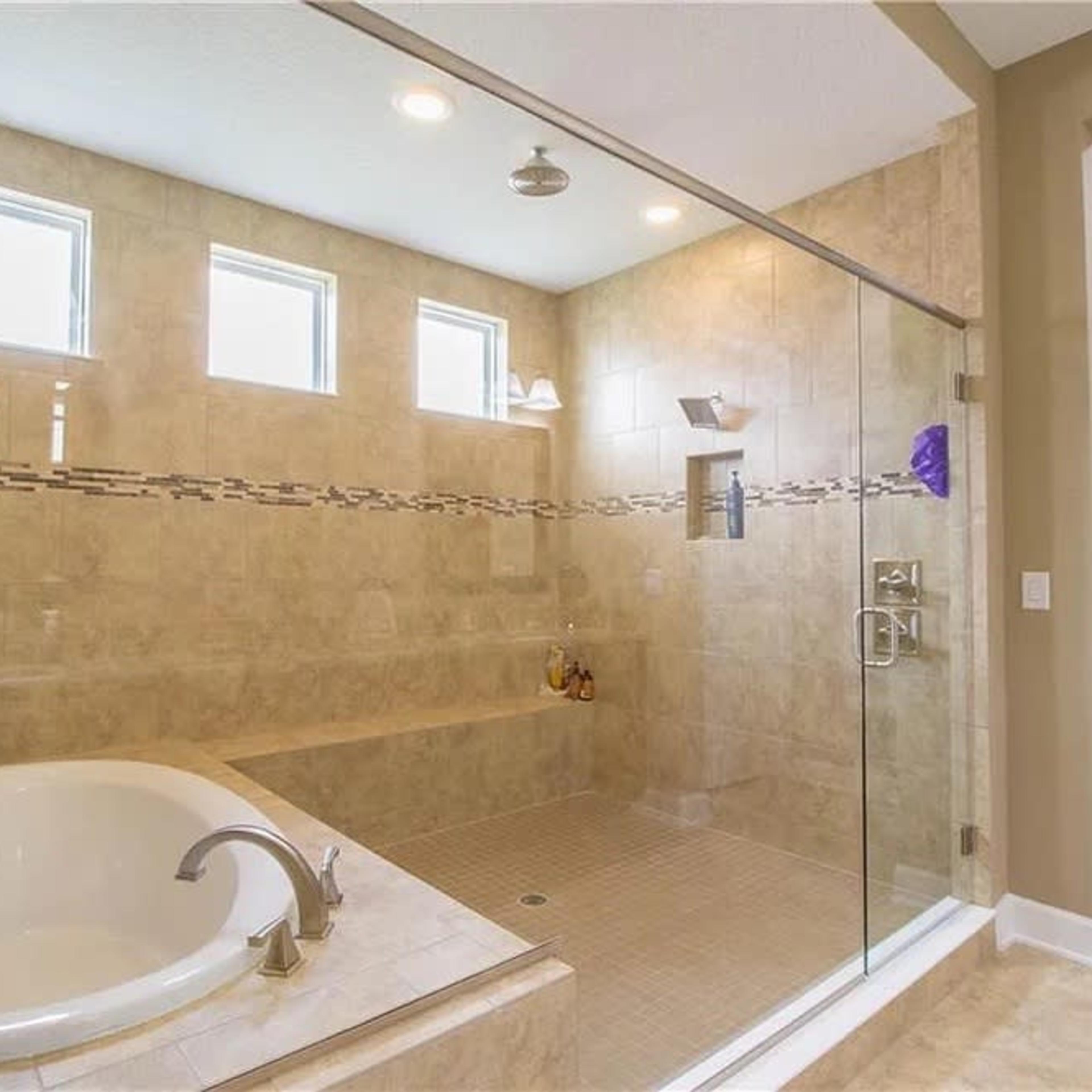 A spacious bathroom featuring a glass-enclosed shower, a white soaking tub, and natural light coming through multiple windows.