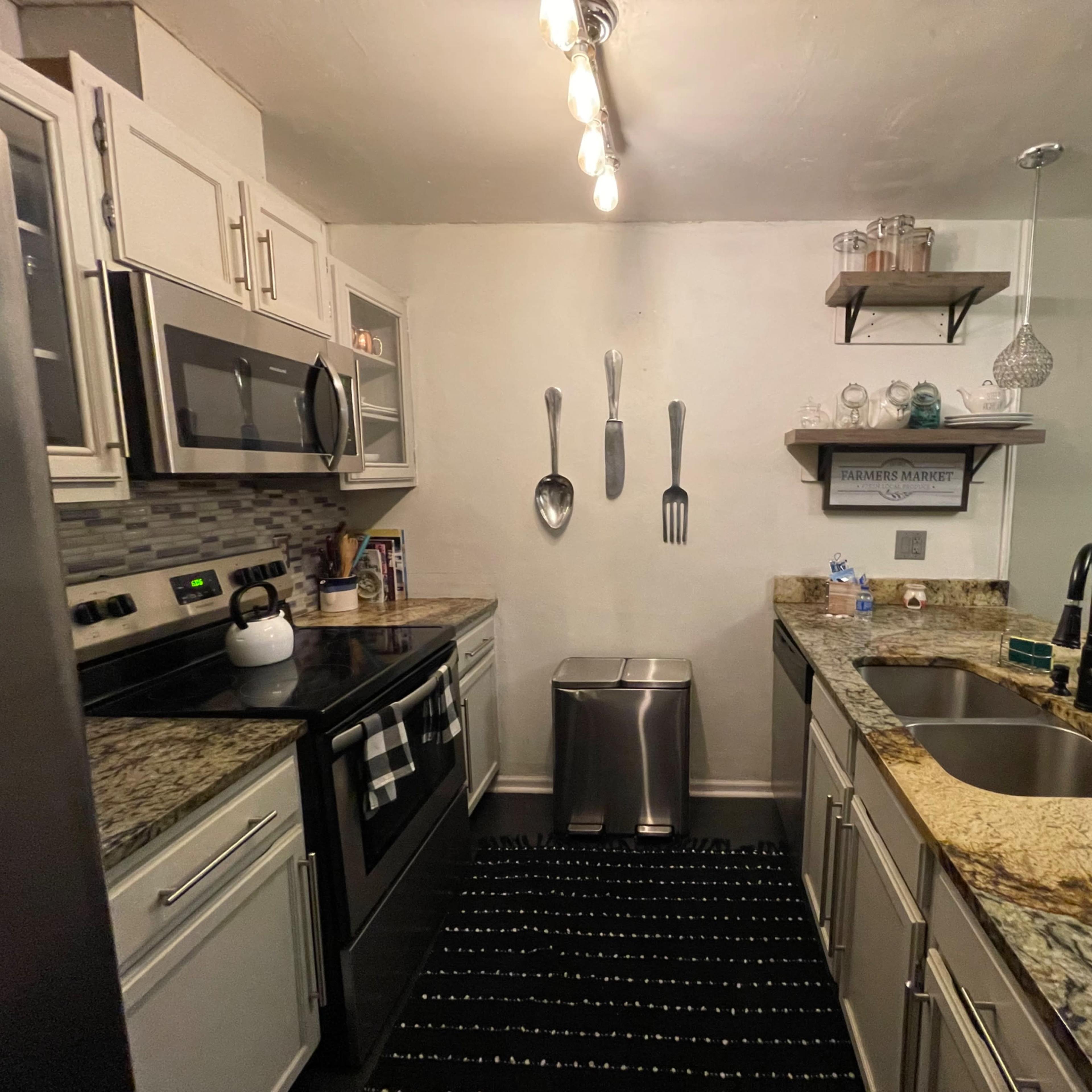 A compact kitchen with stainless steel appliances, granite countertops, and decorative utensils mounted on the wall.