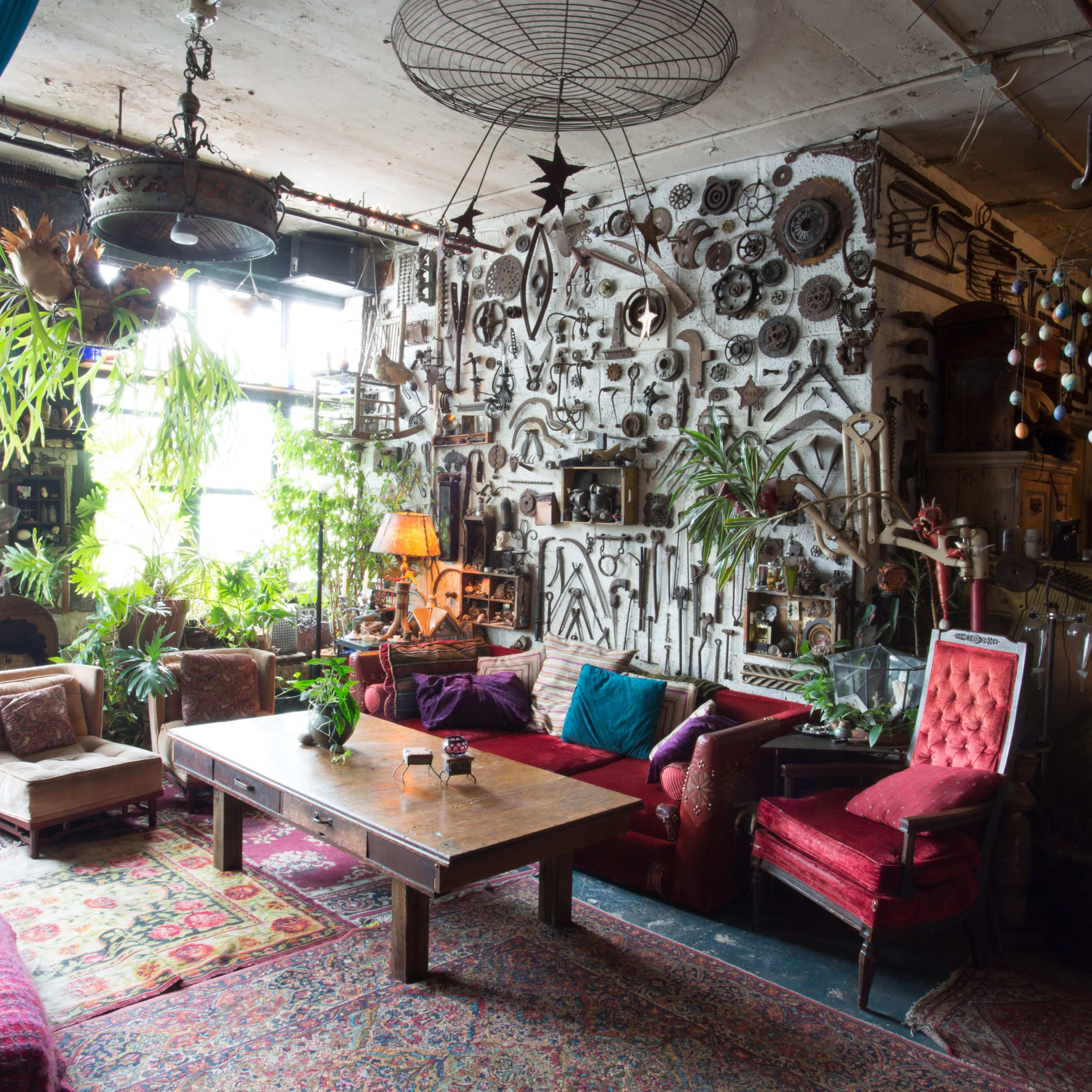 A vintage-style living room filled with eclectic decor, plants, and colorful furniture arranged around a wooden table.