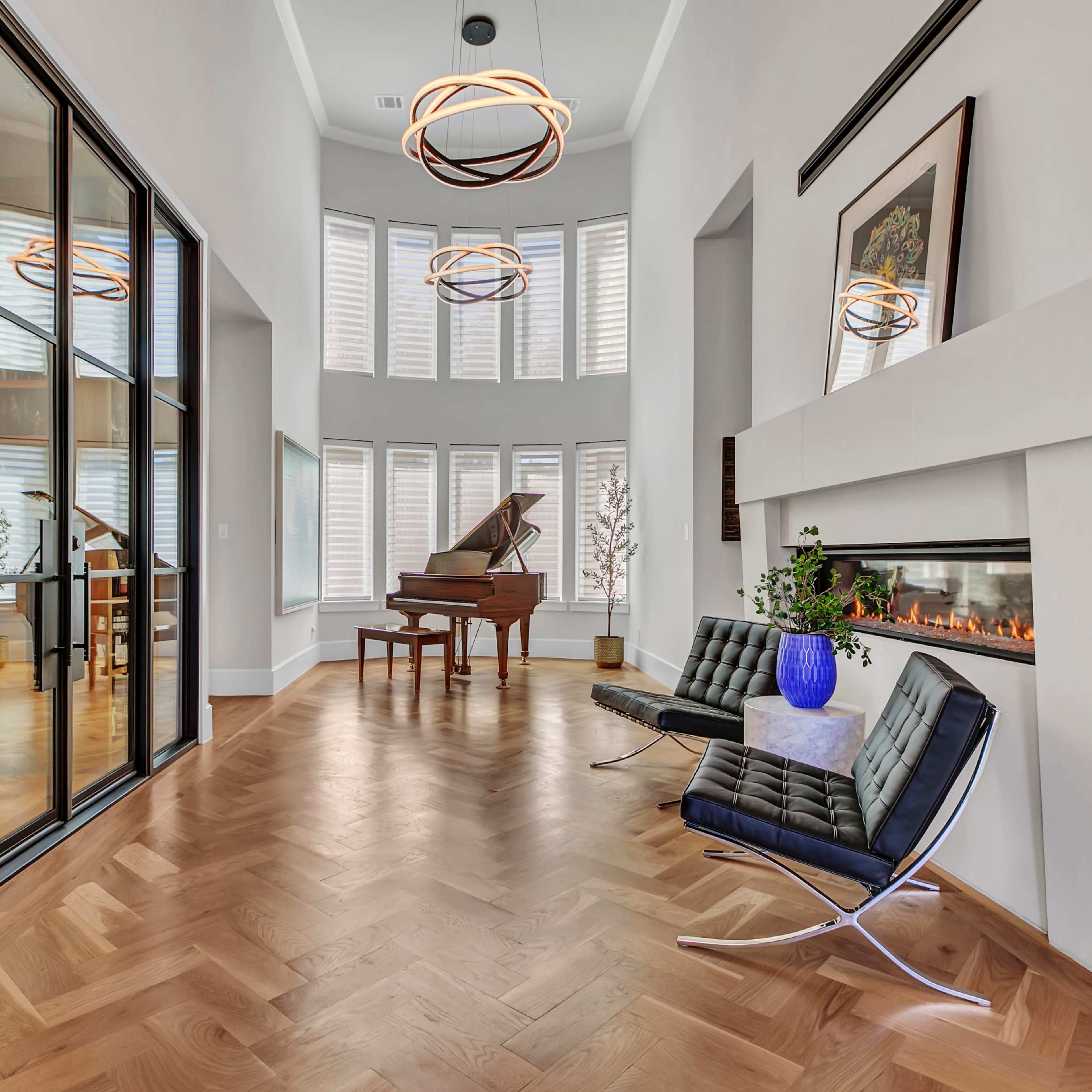 A modern interior features a grand piano, sleek seating, and a fireplace, with large windows allowing natural light to fill the space.