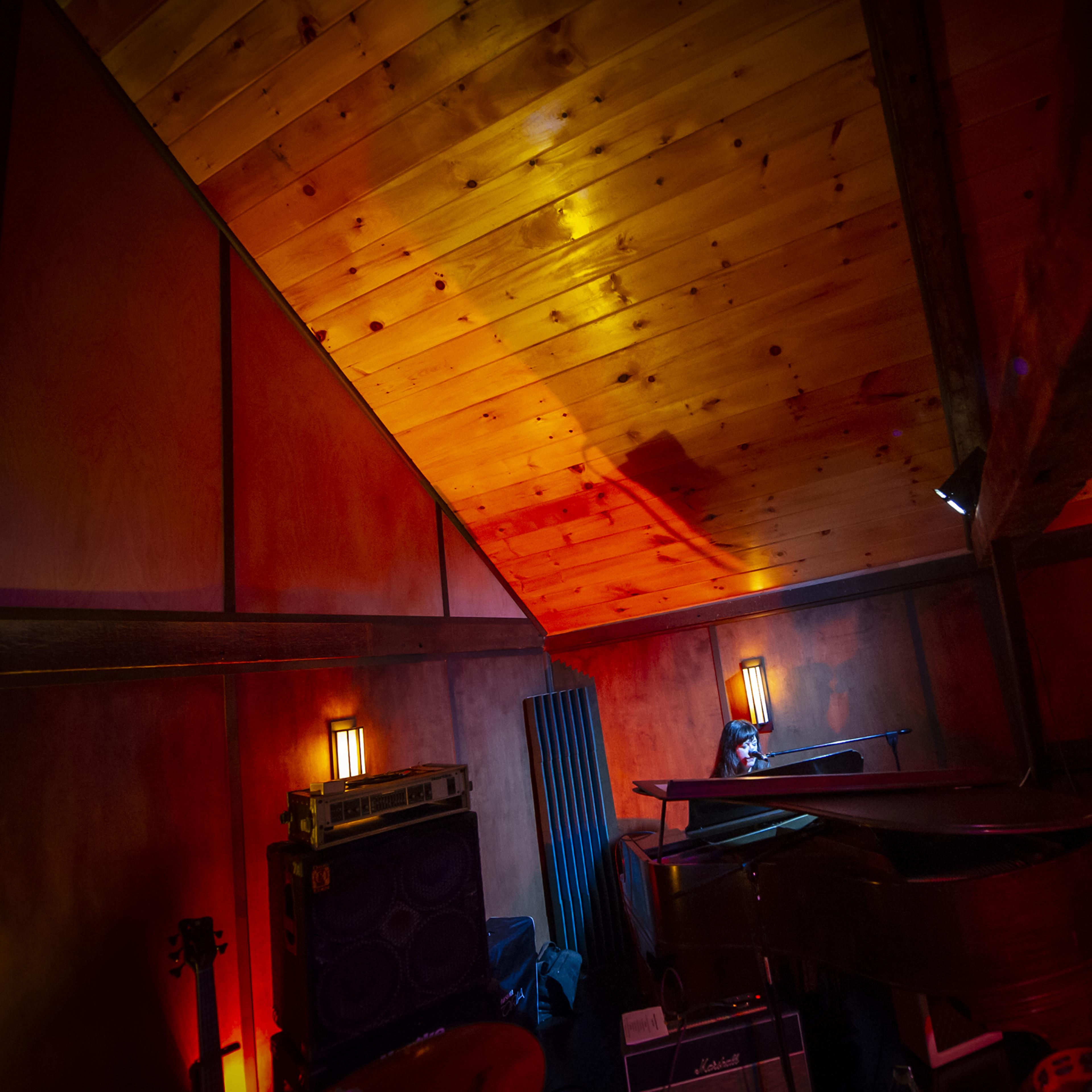 A dimly lit music studio with wooden beams and colorful lighting illuminating various musical instruments and equipment.