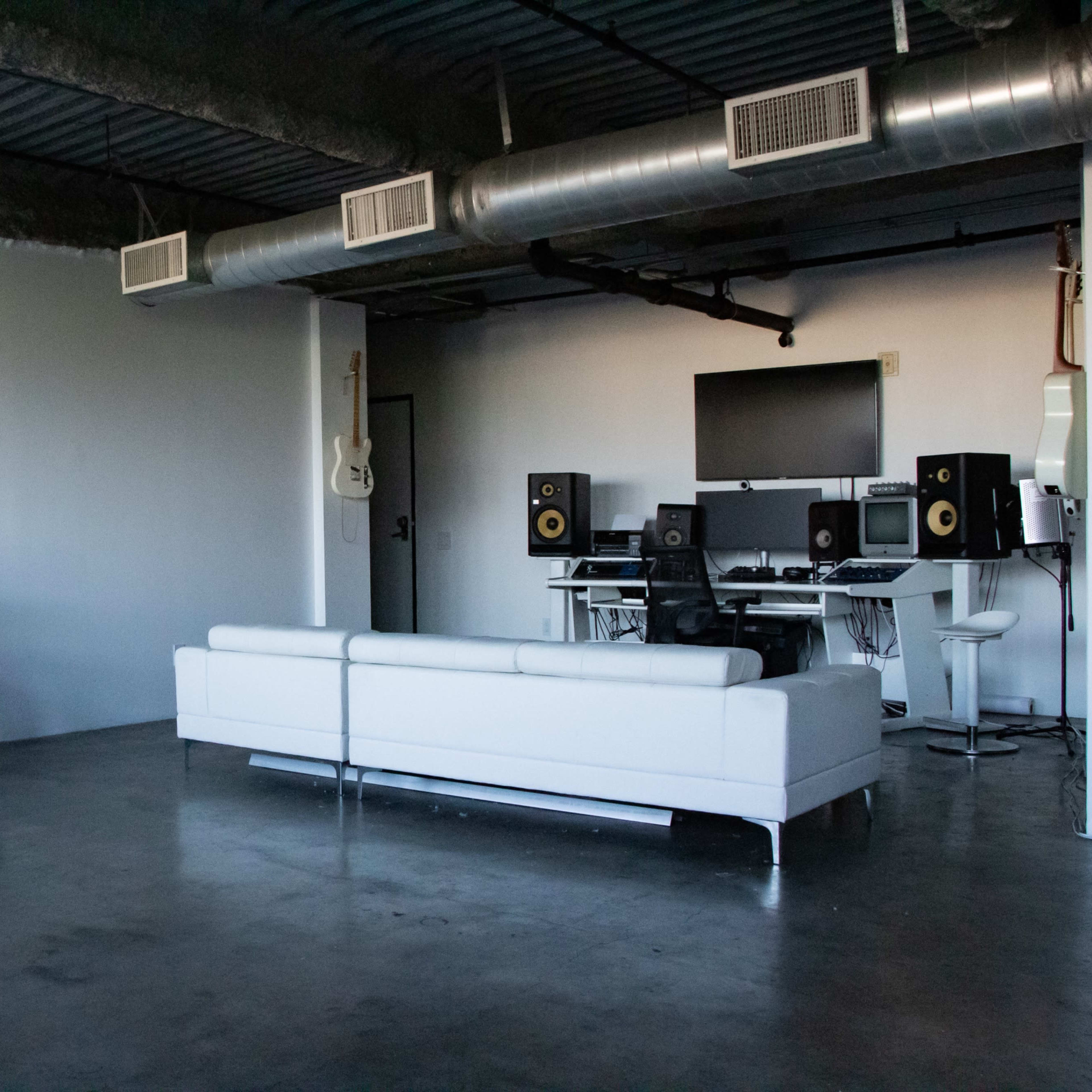 A white dirt bike is parked beside a modern living area featuring a white sofa and a music studio setup with speakers and a computer.