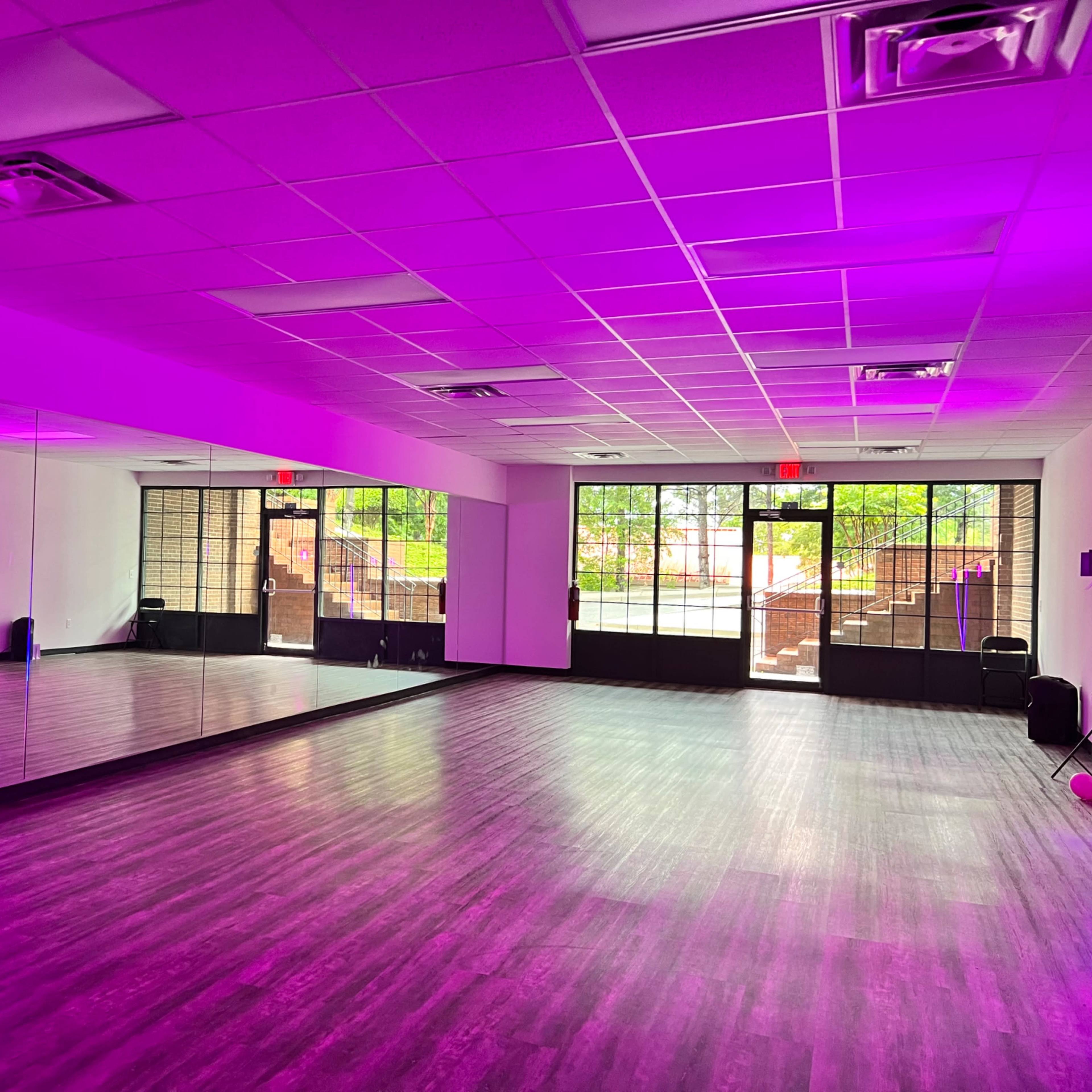 A dance studio with mirrored walls and purple lighting, featuring large windows that open to an outdoor area.