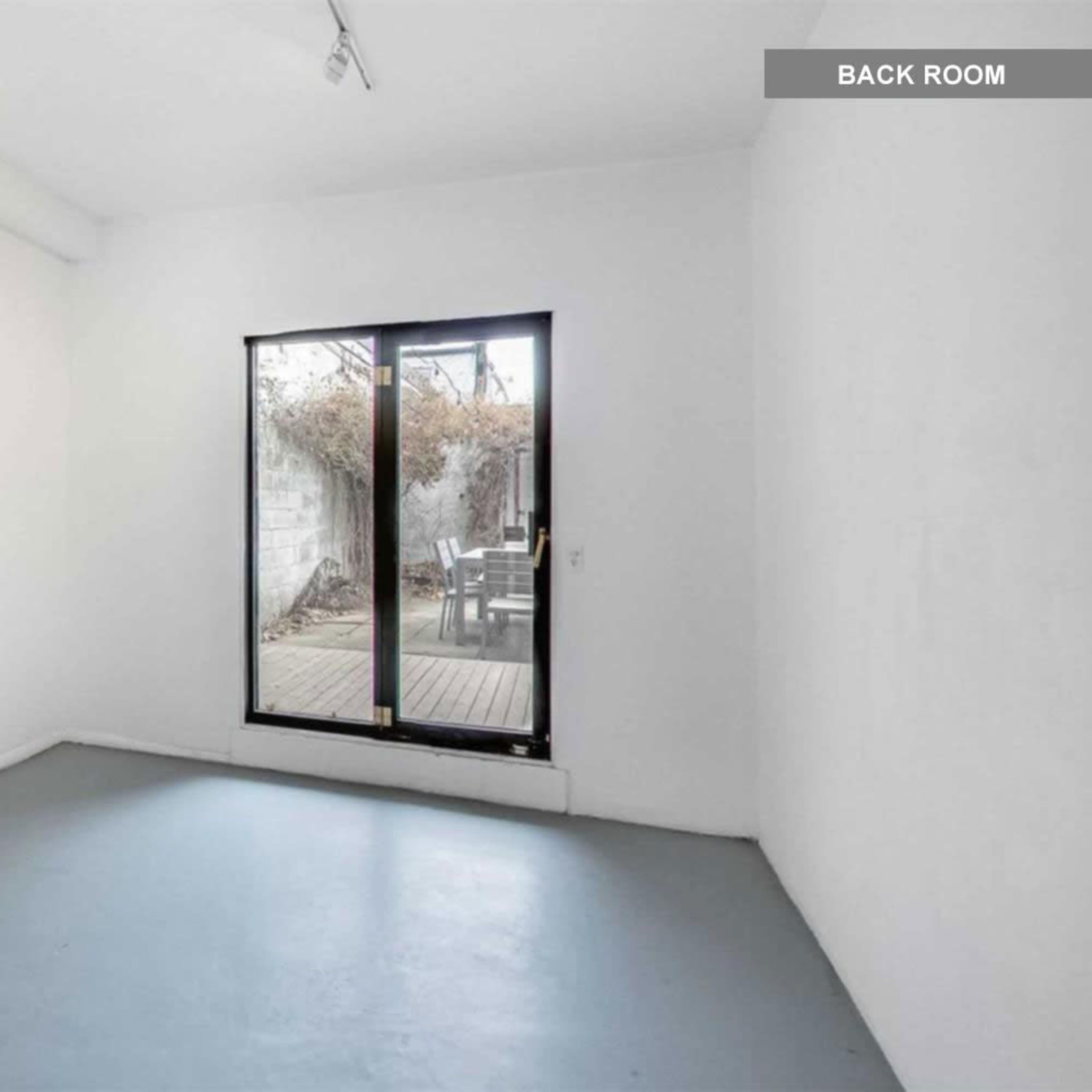 A minimally furnished room with white walls and a large window overlooking a deck area.