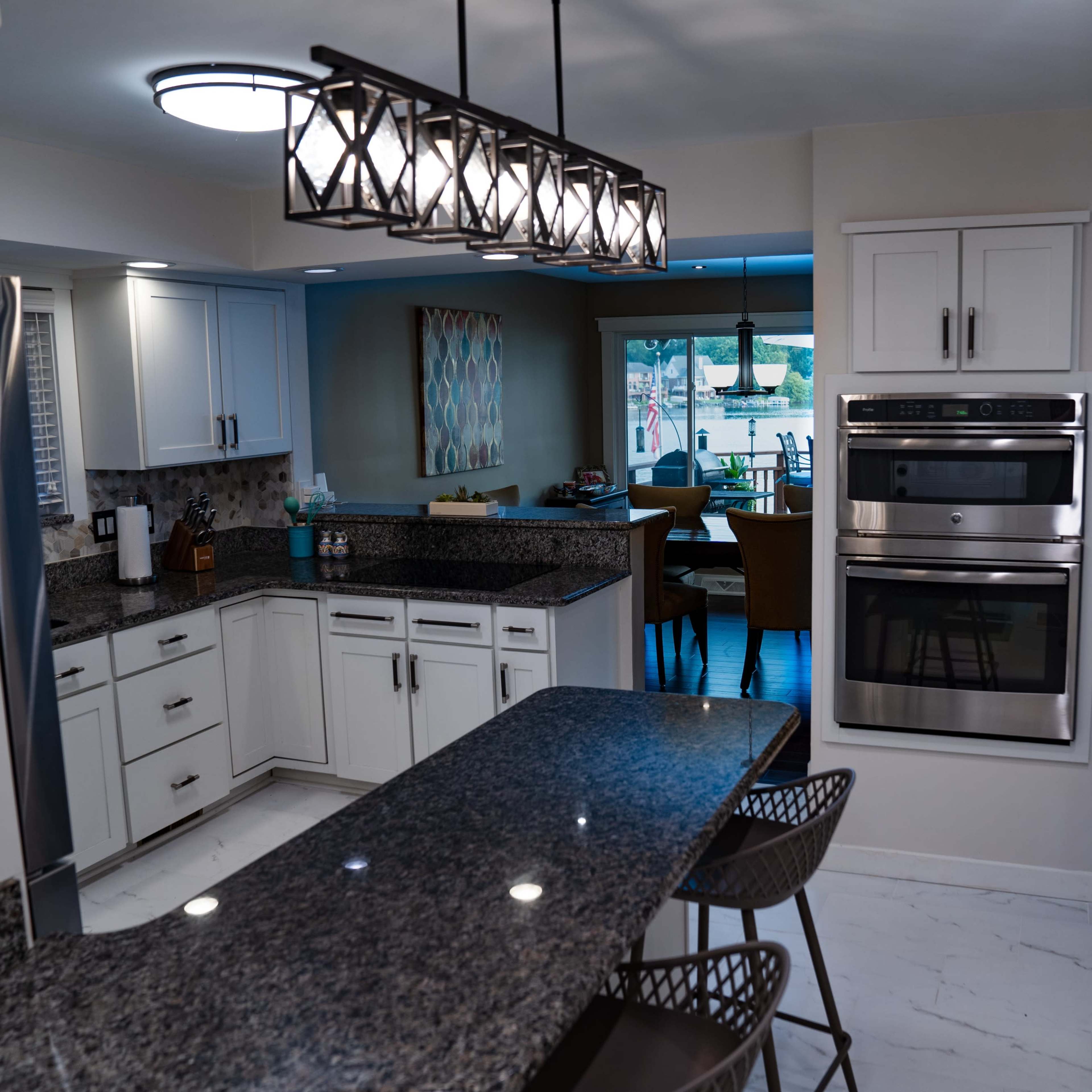 A modern kitchen featuring white cabinetry, a granite countertop island with bar stools, and stainless steel appliances.