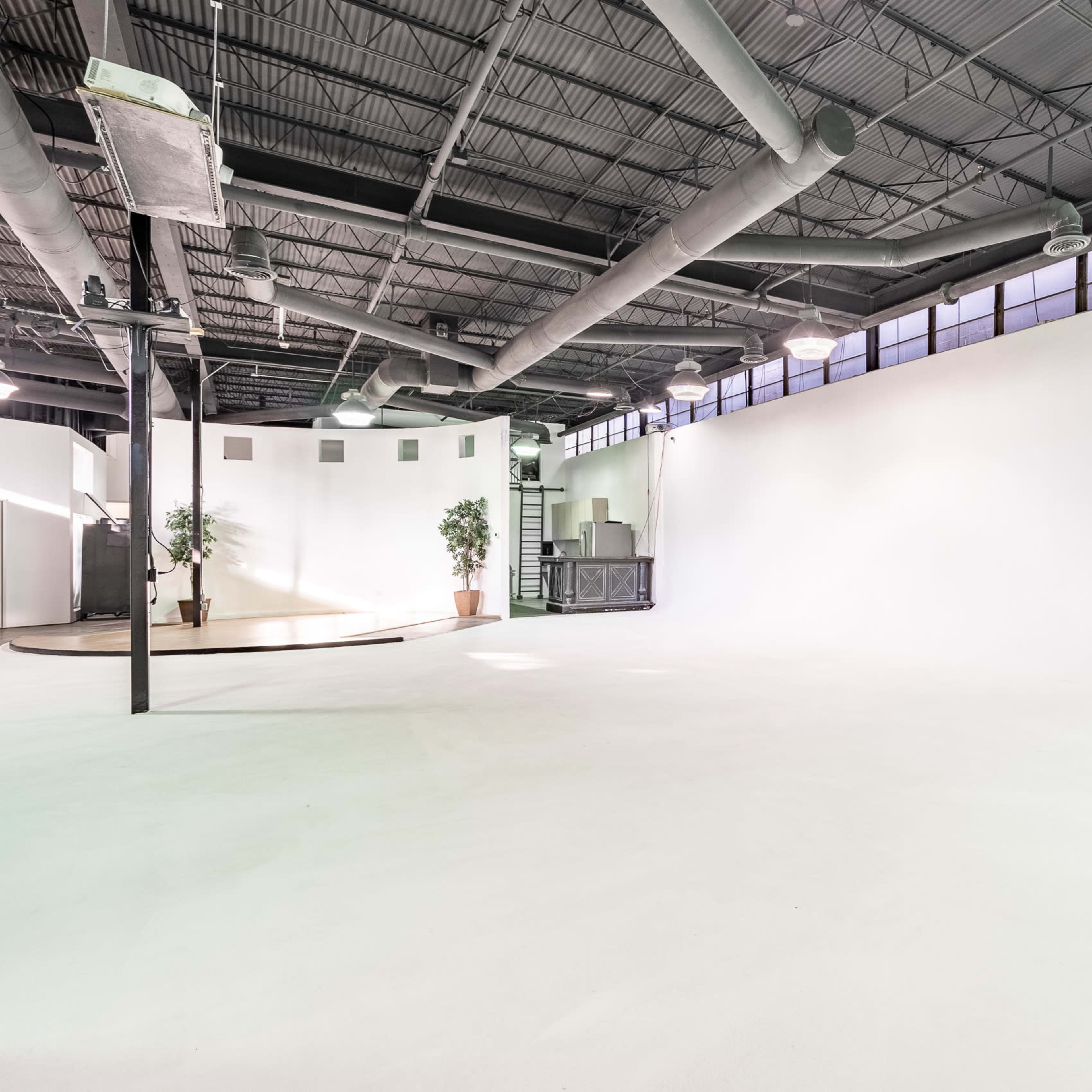 A spacious, empty room with a concrete floor, large windows, and a few potted plants.