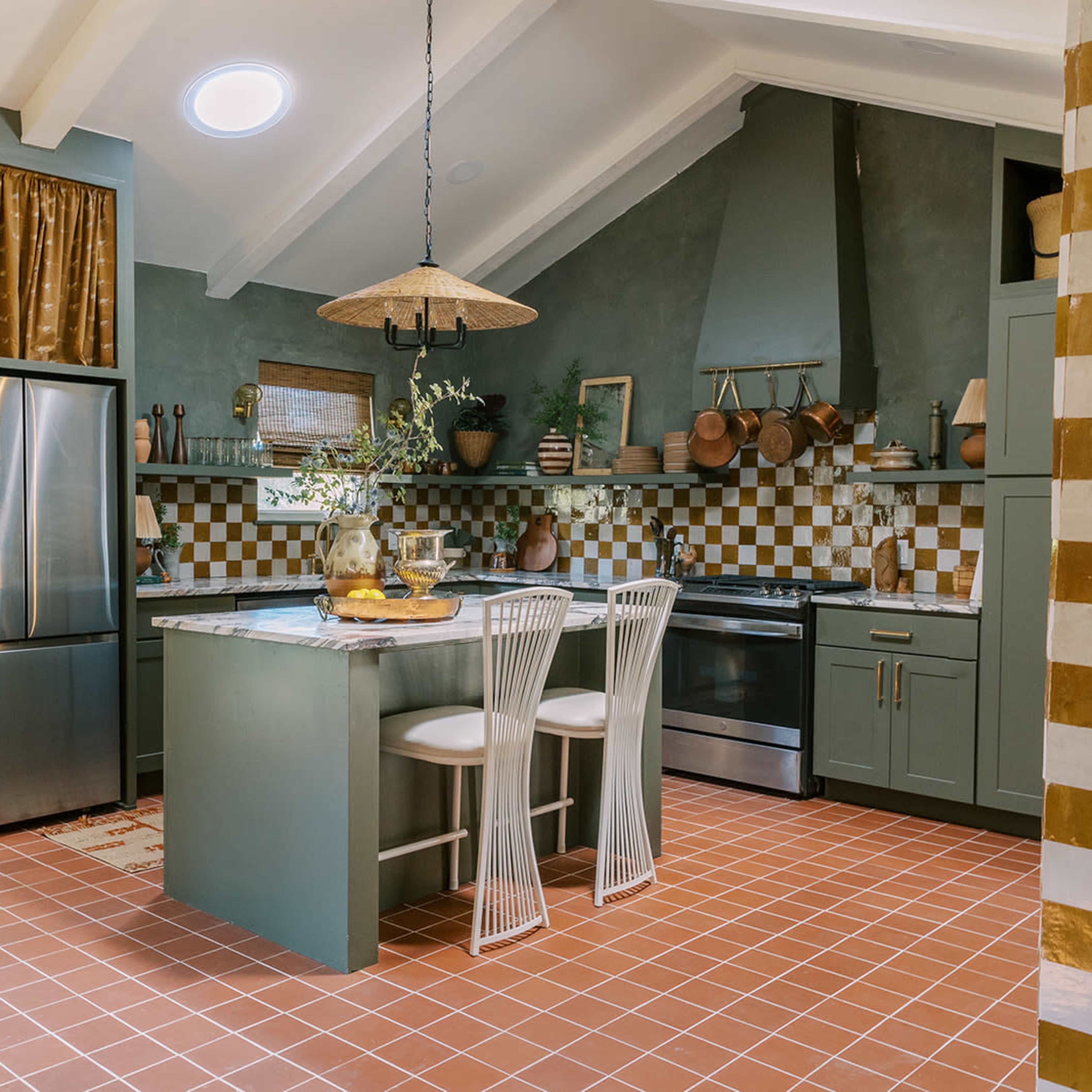 The kitchen features a central island with two bar stools, a stainless steel refrigerator, and a backsplash of patterned tiles.