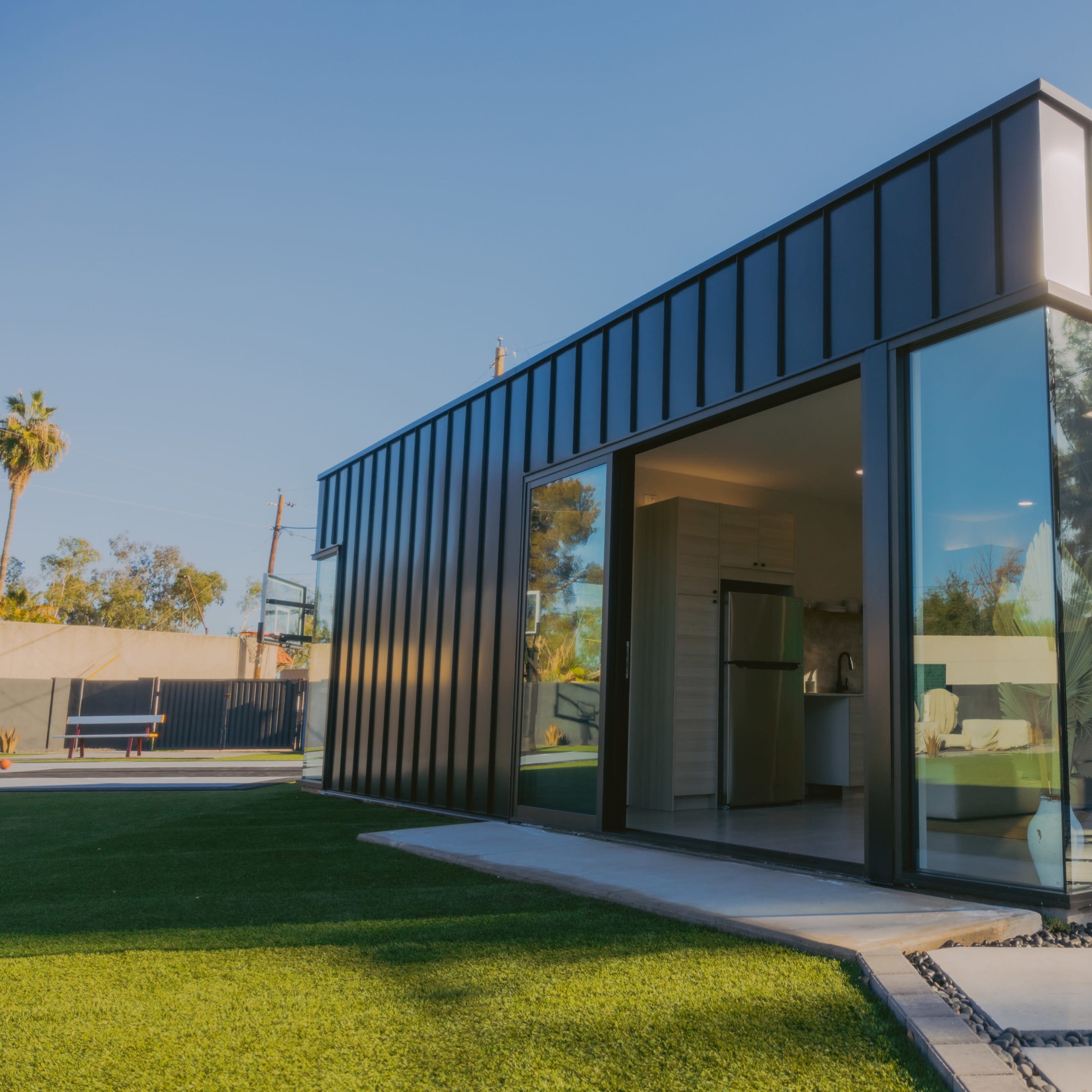 A modern black metal house features large glass walls and a landscaped yard with artificial turf.