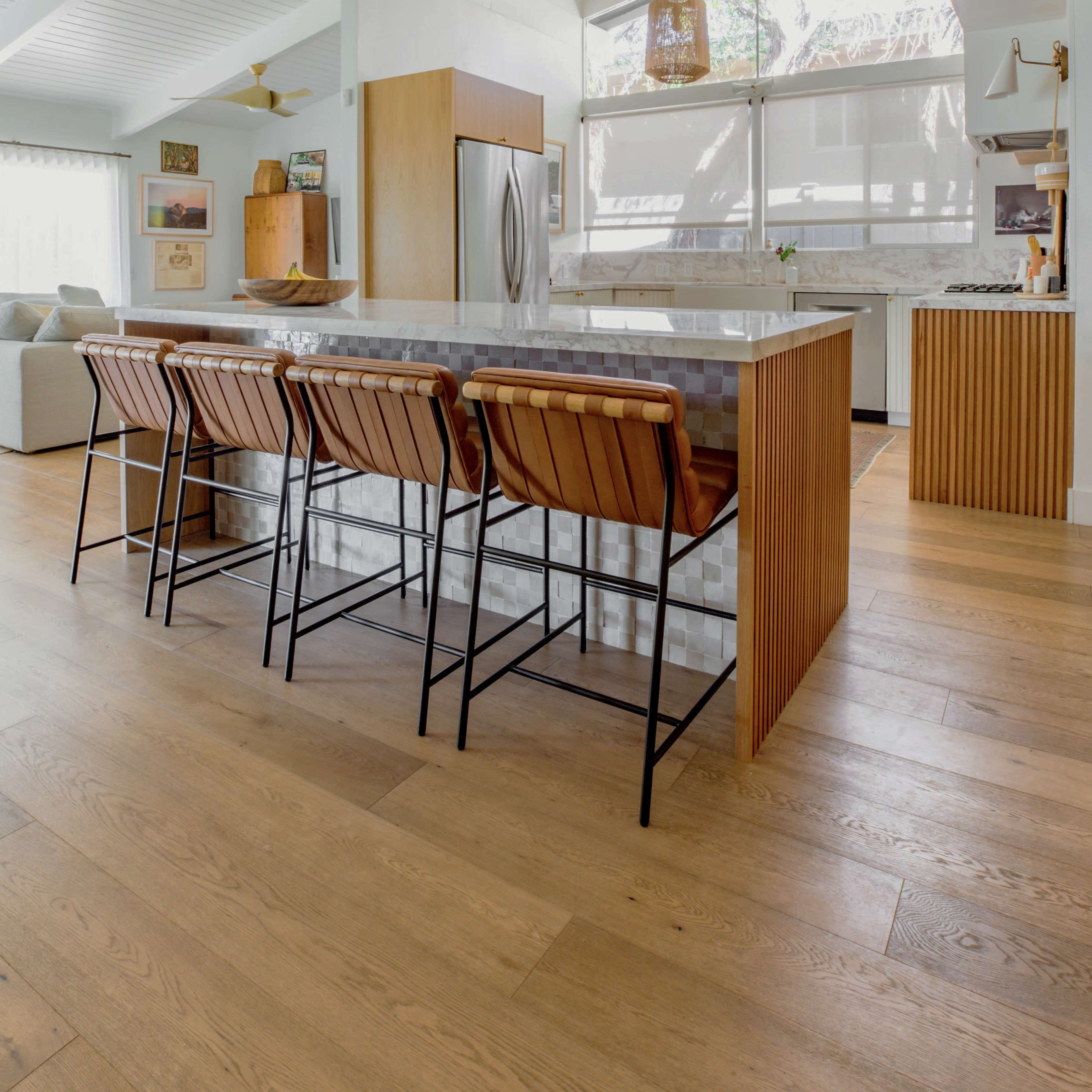 A modern kitchen features a marble island with four metallic bar stools and large windows that provide natural light.