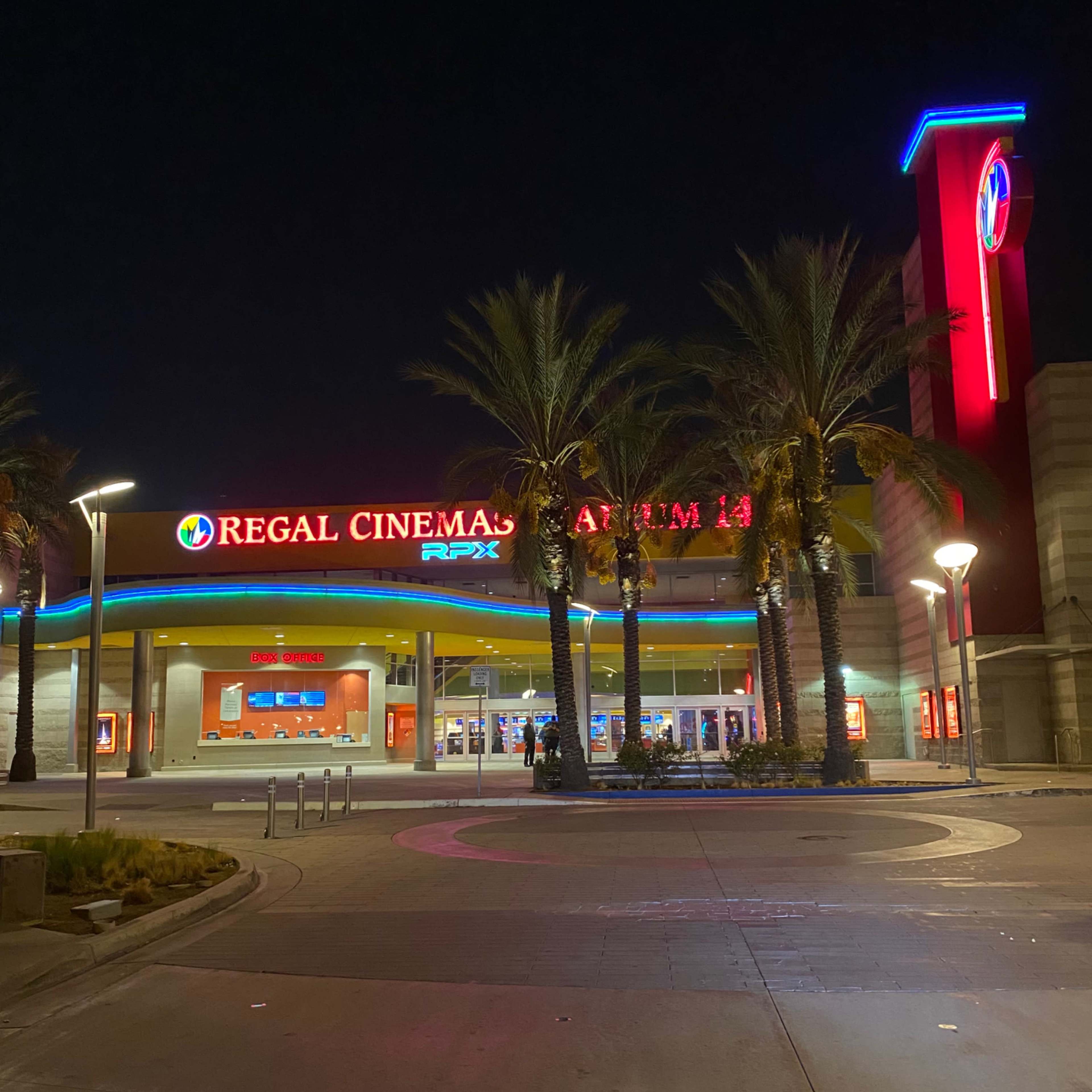 The brightly lit entrance of the Regal Cinemas At The Spectrum 14 is flanked by palm trees at night.