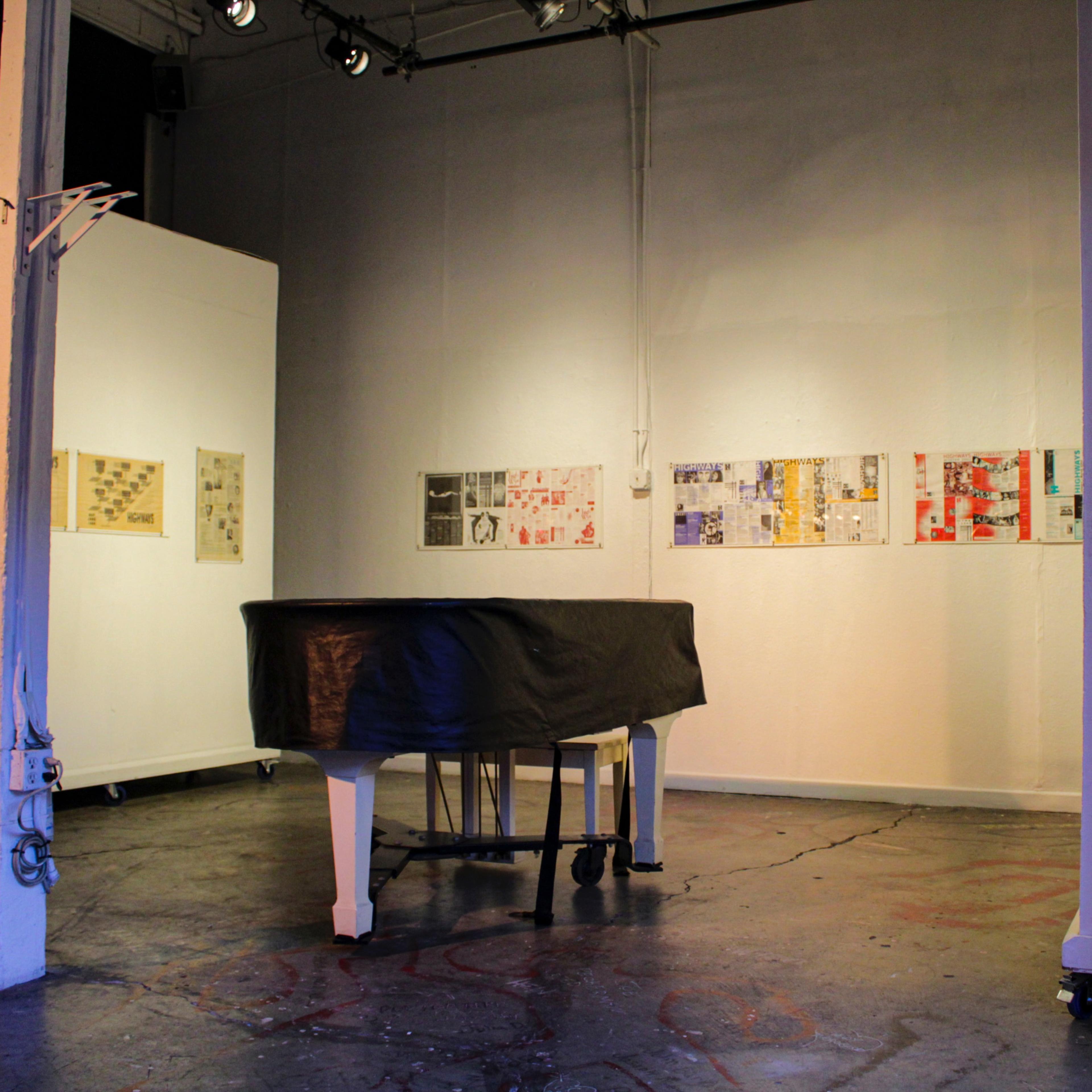 An art gallery with a covered piano in the foreground and framed artworks displayed on the walls.