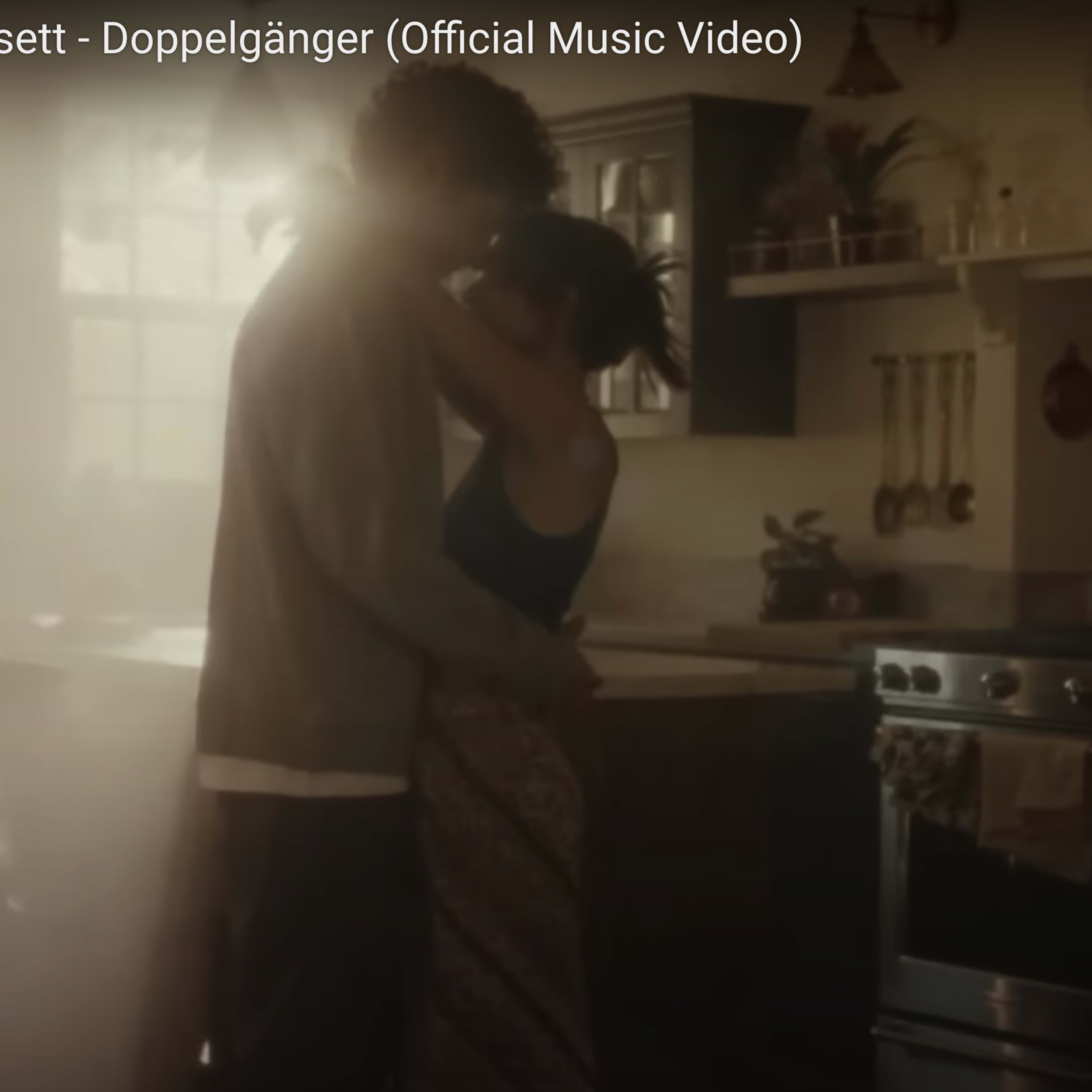 A couple embraces in a softly lit kitchen, surrounded by warm shadows.
