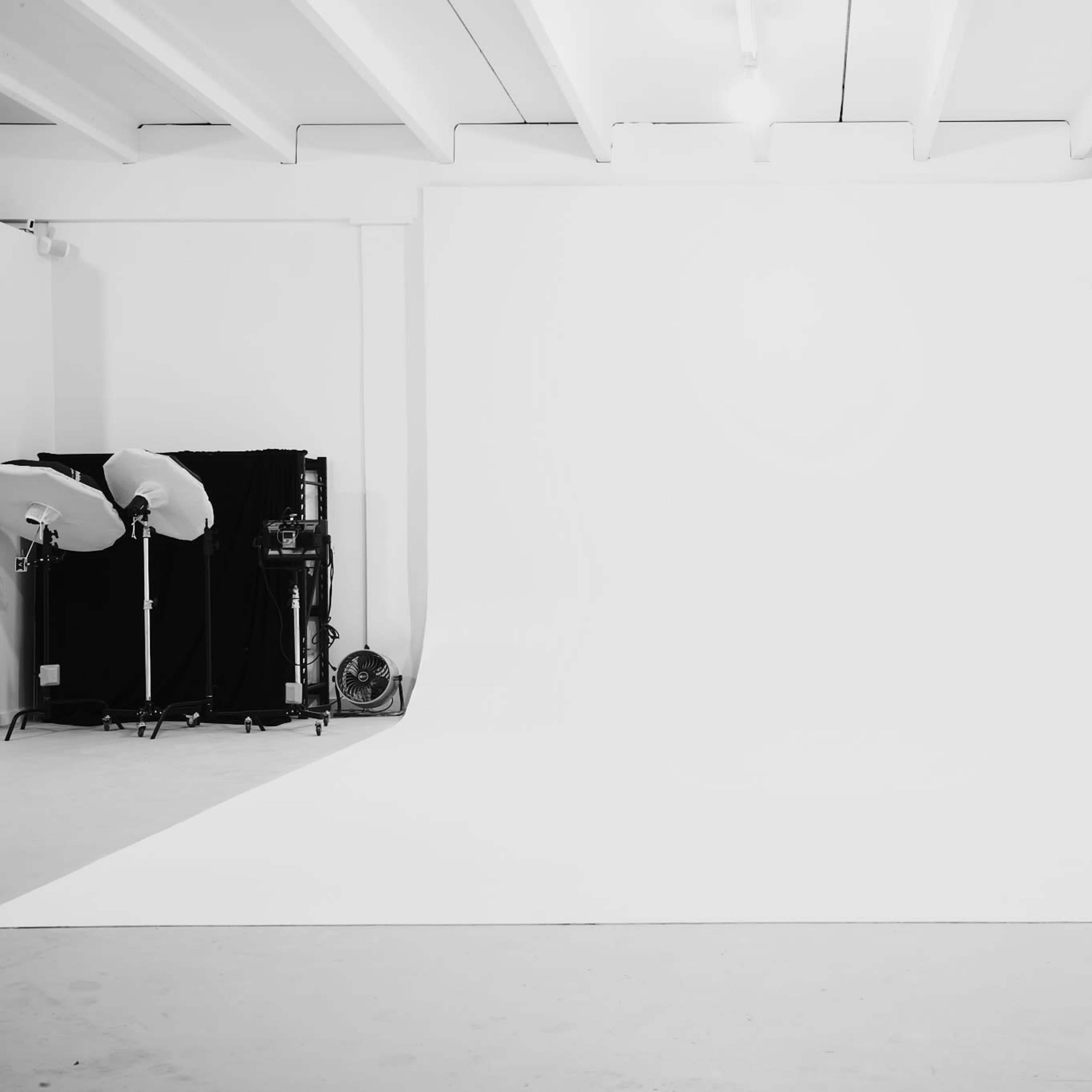 A photography studio with a large, white seamless backdrop and studio lighting equipment arranged to the side.