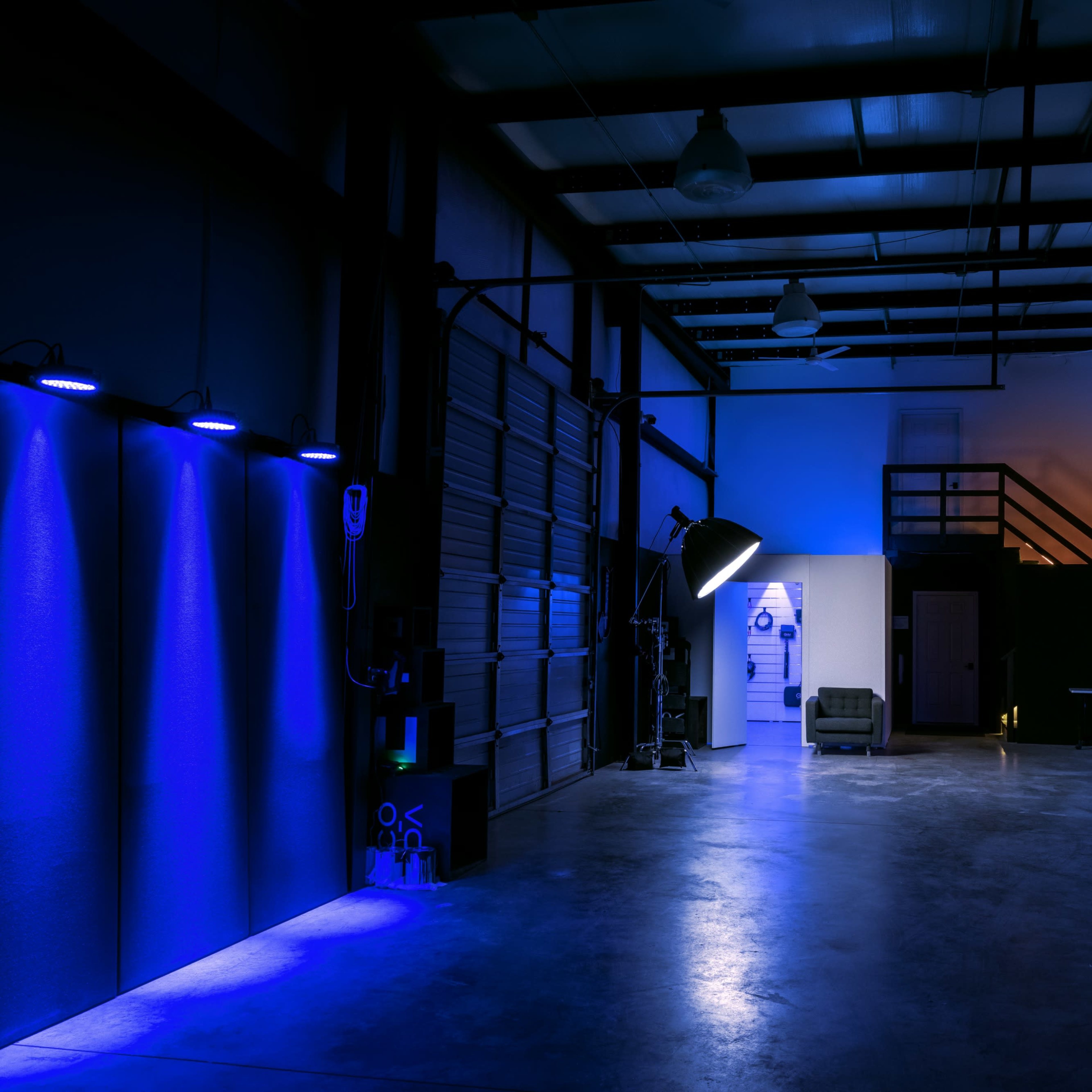 A spacious, dimly lit industrial studio featuring blue lighting, a couch, and various photographic equipment.