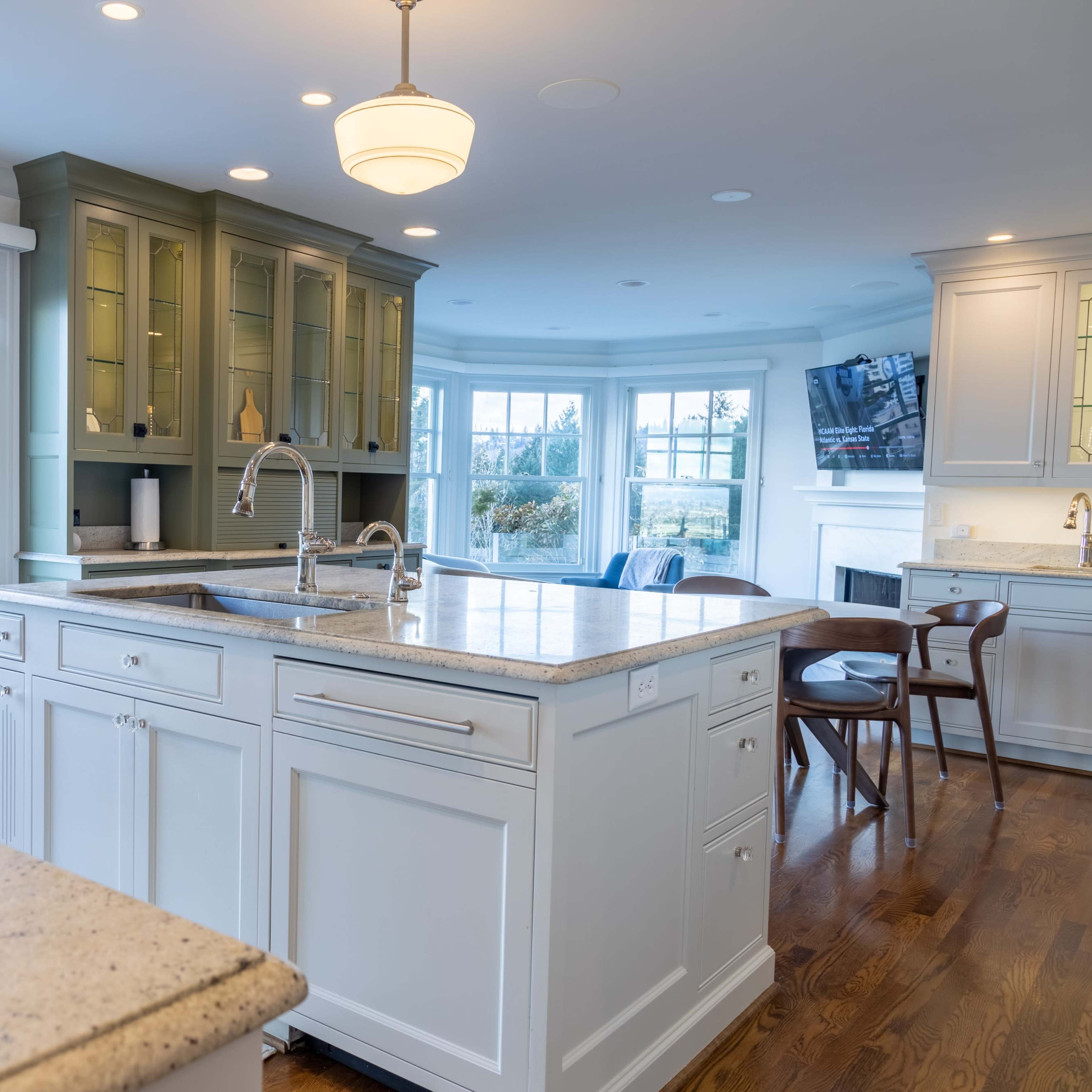 A well-lit kitchen featuring a central island with a countertop, a green cabinet against the back wall, and large windows offering a view of the city.