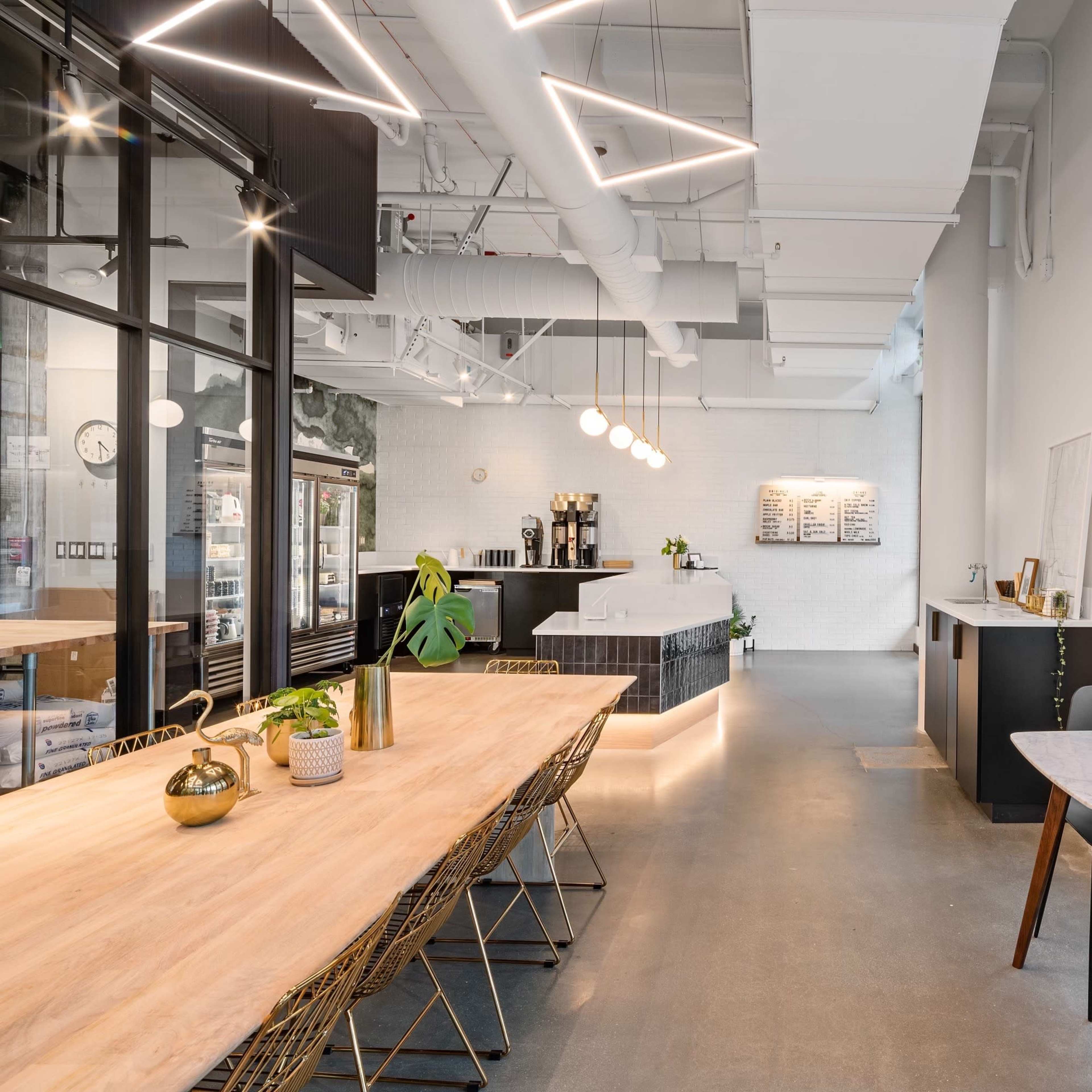 A modern café interior featuring a long wooden table, stylish chairs, and large windows that provide natural light.